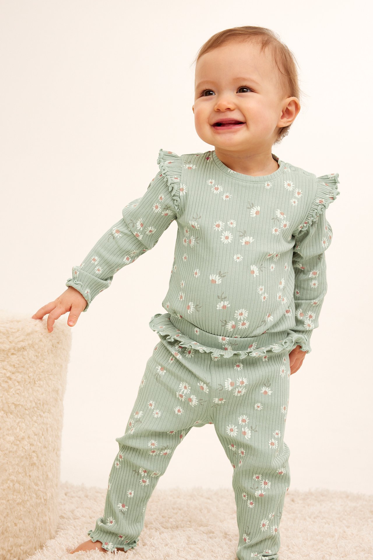 Frontvy av en baby i grön ribbad topp och matchande leggings med volanger och blommigt tryck.