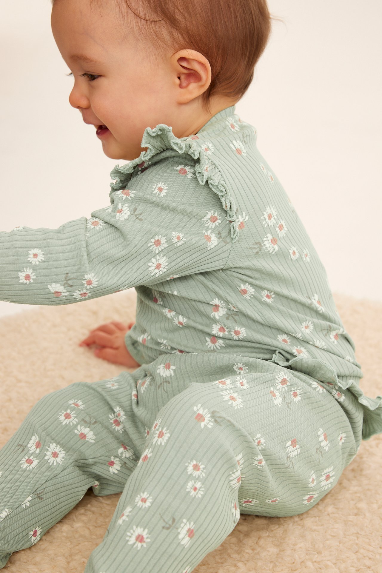 Sidovy av en baby i gröna ribbade blommiga leggings och matchande långärmad topp med volanger.
