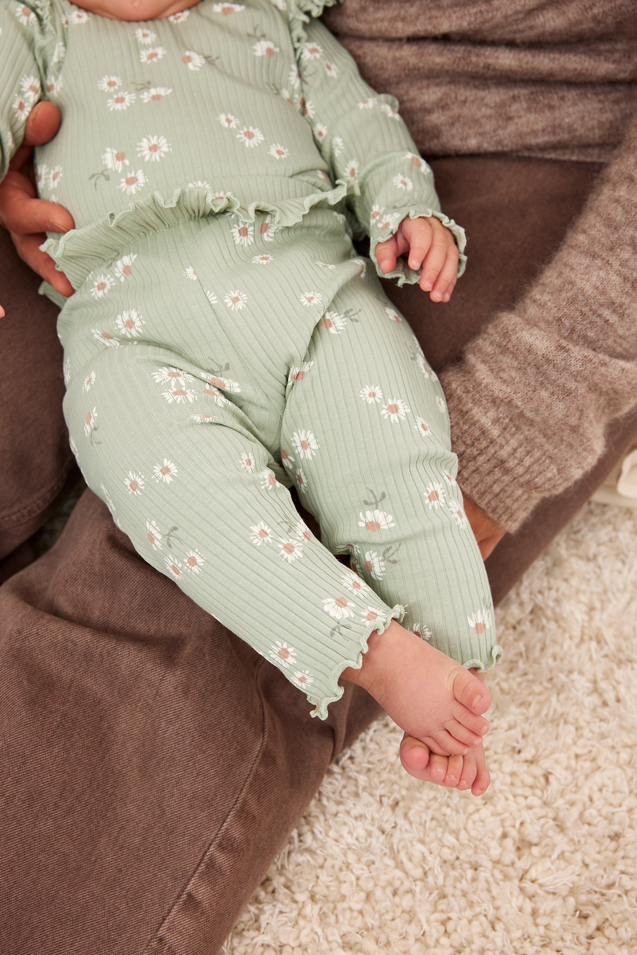 Närbild på en baby i ljusgröna ribbade blommiga leggings och matchande topp med volangdetaljer.