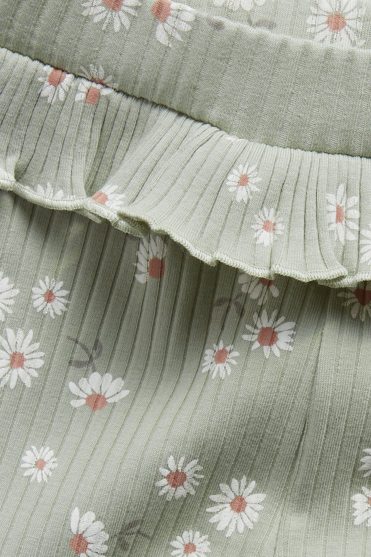 Närbild på gröna ribbade baby leggings med volang och vitt blommönster.