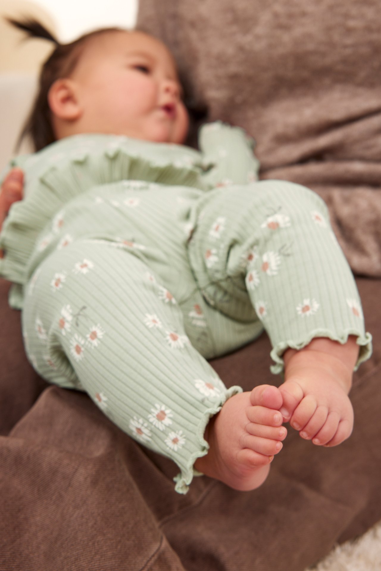 Närbild på baby i gröna ribbade blommiga leggings med volangdetaljer och matchande topp.