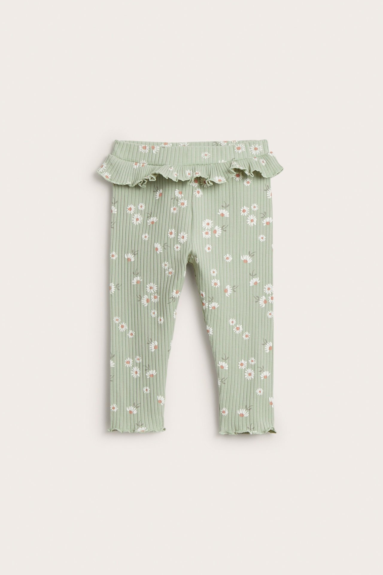 Frontvy av babyribbade ljusgröna leggings med volang i midjan och vitt blommönster.