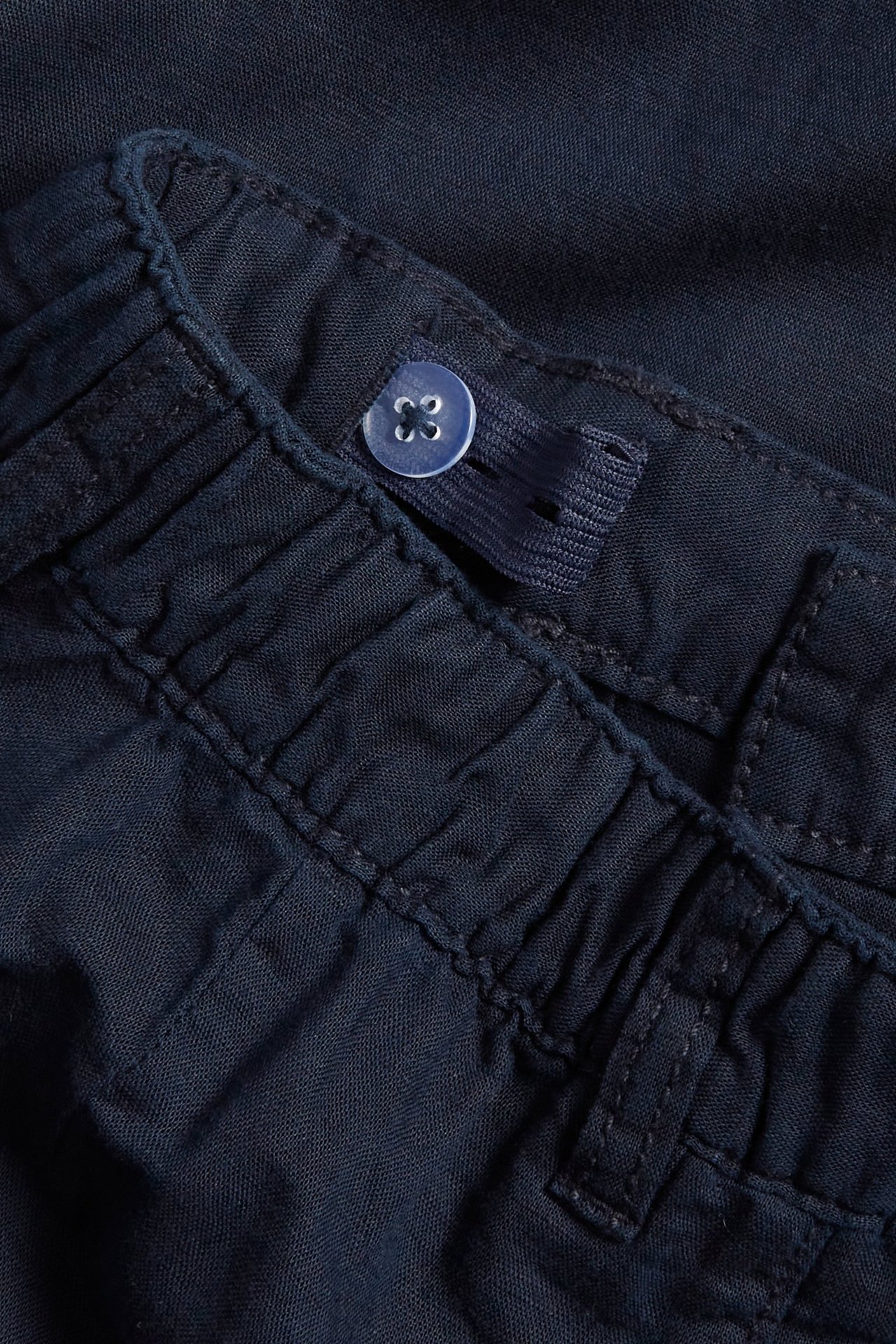 Zbliżenie na granatowe spodnie dziecięce z mieszanki lnu, z elastyczną talią i regulowanym guzikiem.