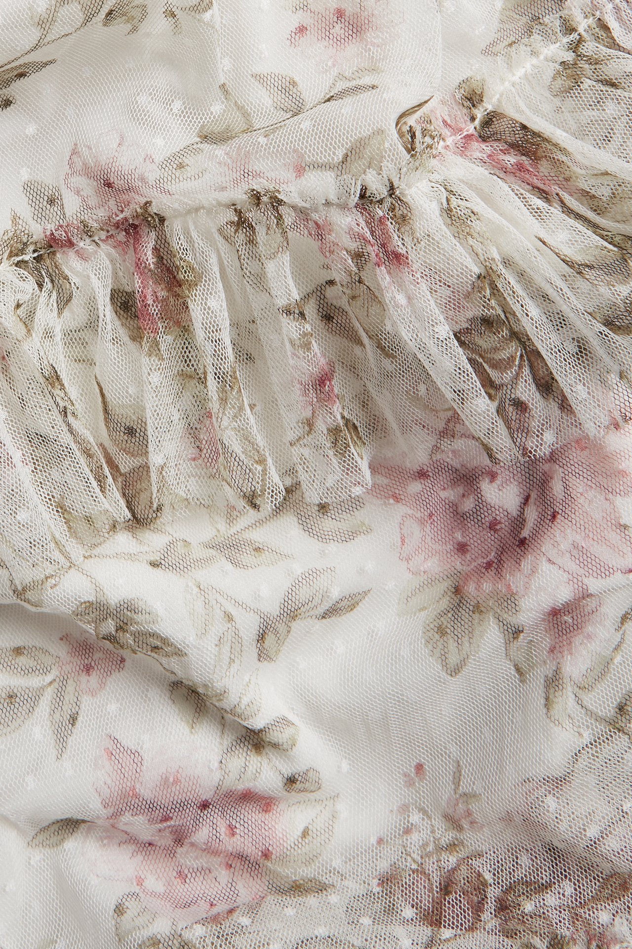 Närbild av en offwhite meshklänning med rosa blommigt mönster, strukturprickar och volanger.