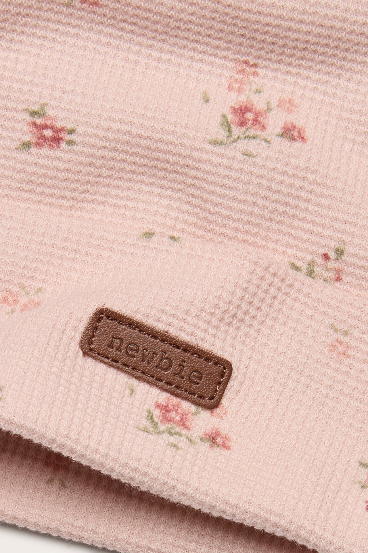 Nærbilde av en lys rosa blomstret jerseylue med oppbrett og brunt 'newbie'-merke.