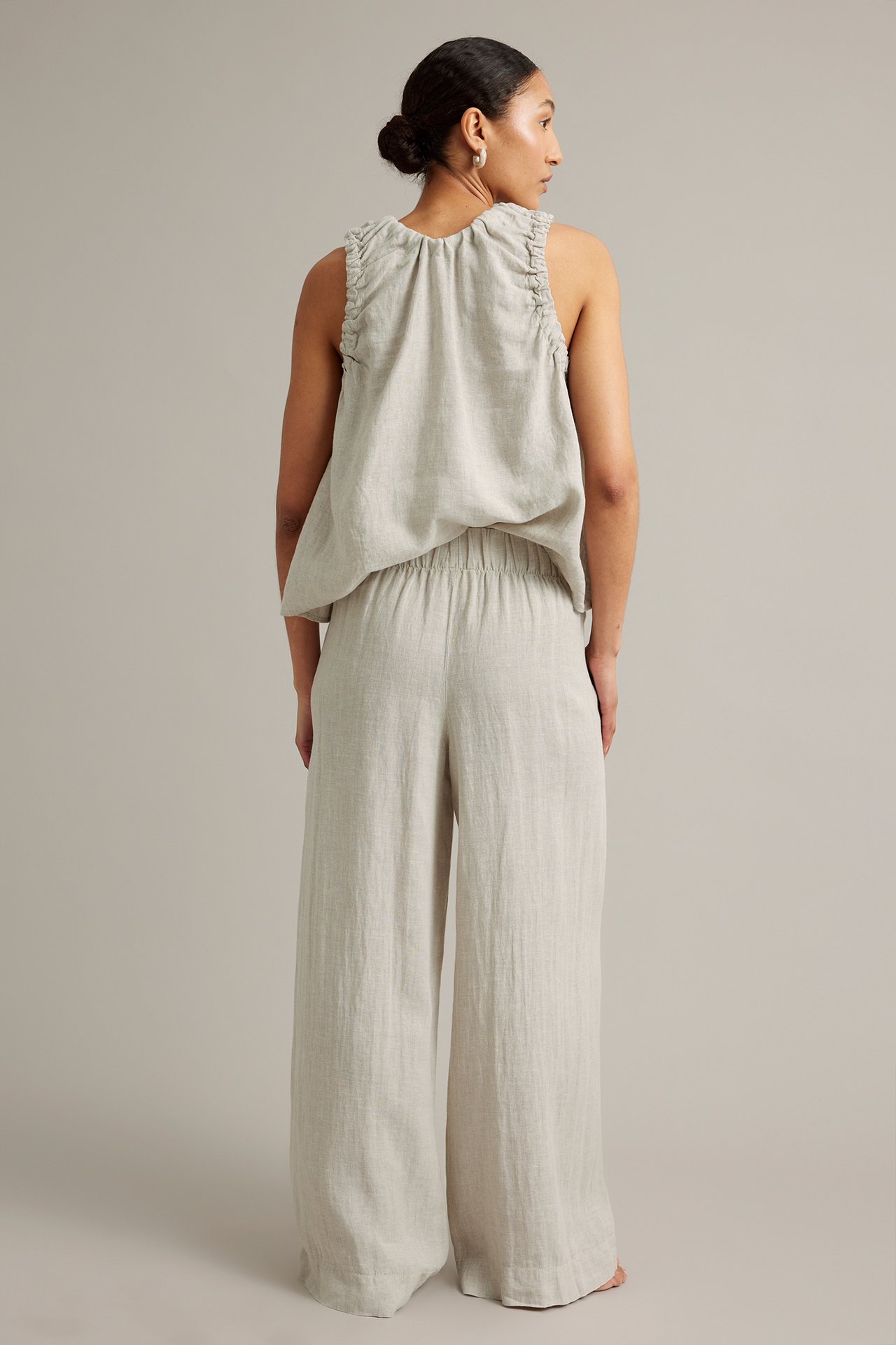 Naisen takakuva leveissä beigenvärisissä pellavahousuissa ja yhteensopivassa röyhelötopissa.