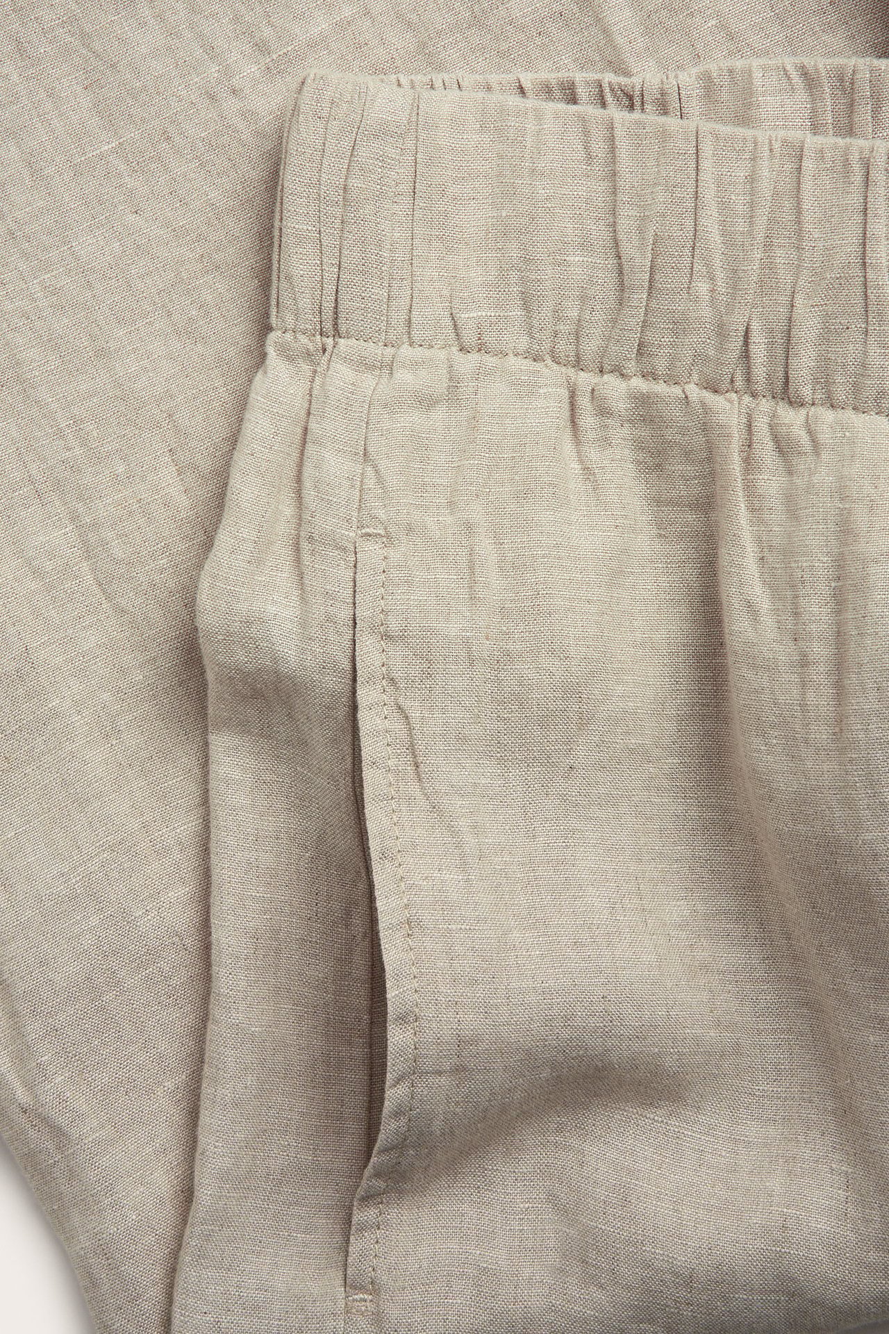 Zbliżenie beżowych melanżowych spodni lnianych z elastyczną talią i boczną kieszenią.