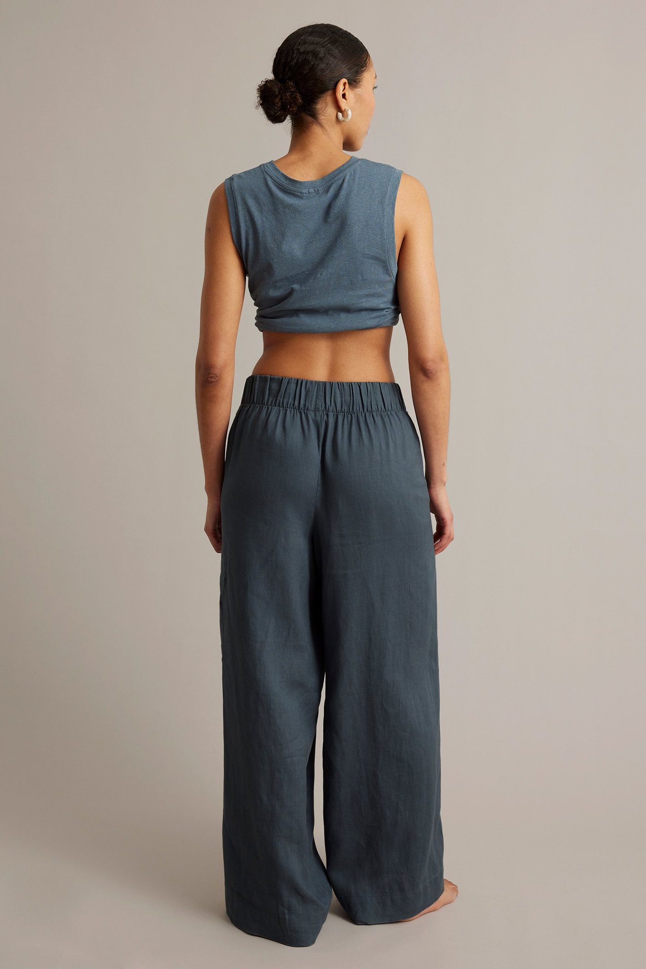Bakifrån på kvinna i mörkblå vida linnebyxor med resår i midjan och matchande kort linne.
