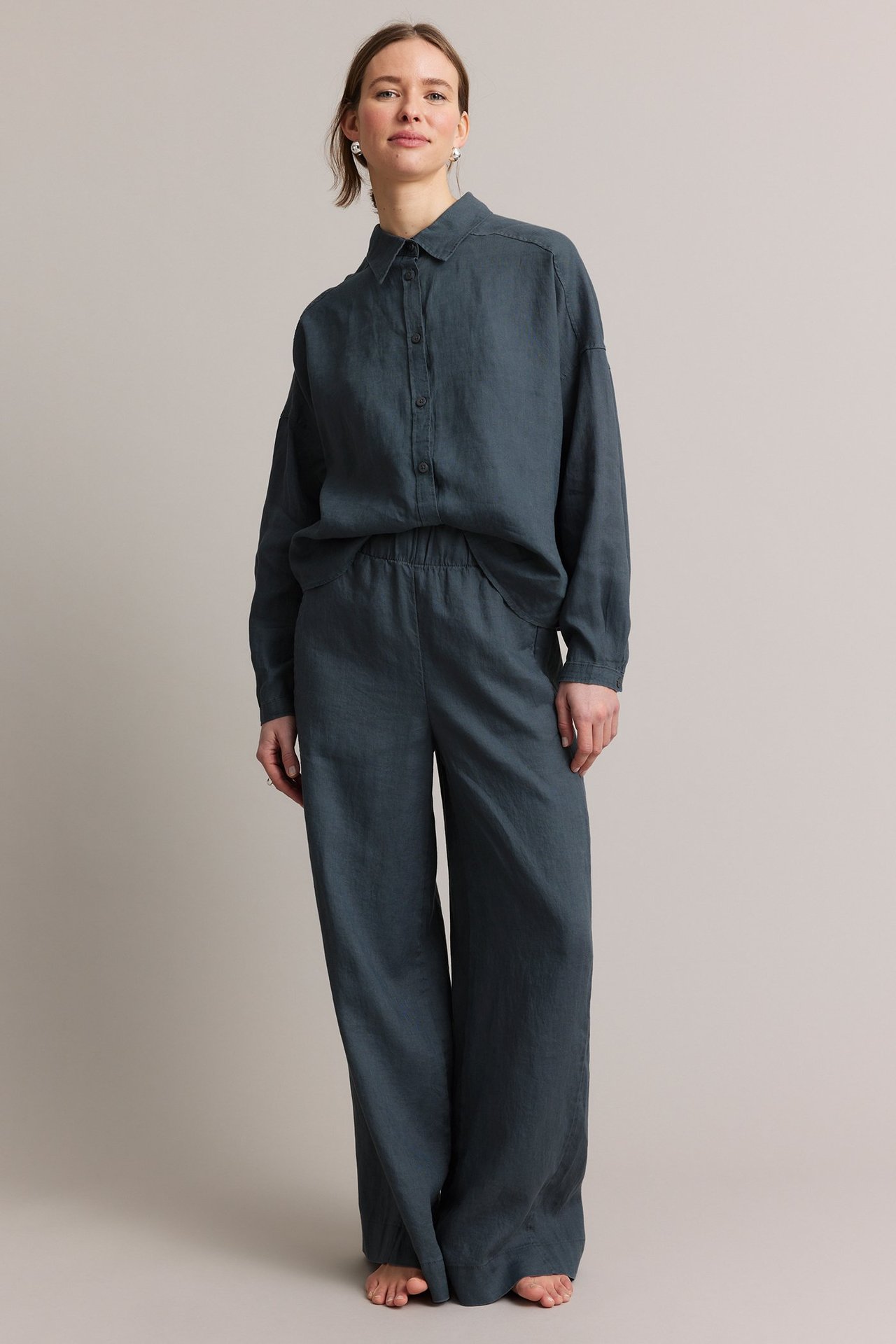 Framifrån: Kvinna i blå linnebyxor med raka ben, resår i midjan och matchande blå linneskjorta.