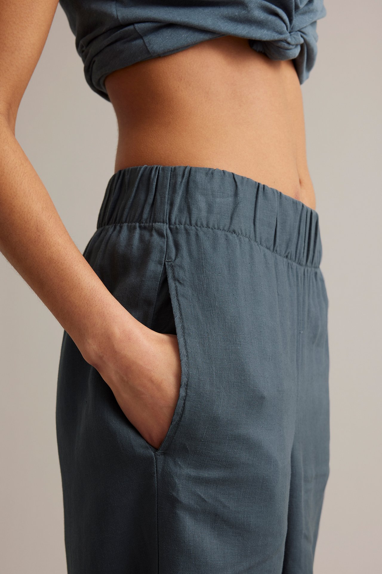 Sidebilde: kvinne i blå vid linbukse, strikk i livet, sidelomme, hånd i. Matchende crop top.