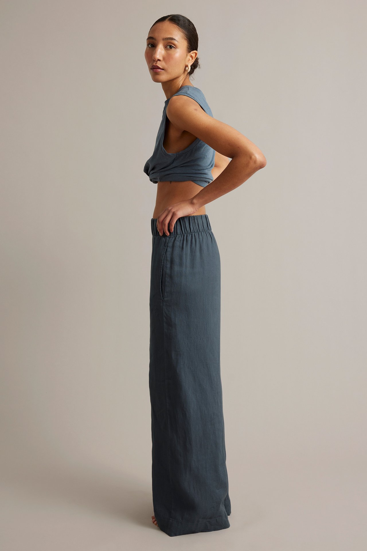 Sivukuva naisesta sinisissä leveälahkeisissa pellavahousuissa joustovyötäröllä ja crop topissa.