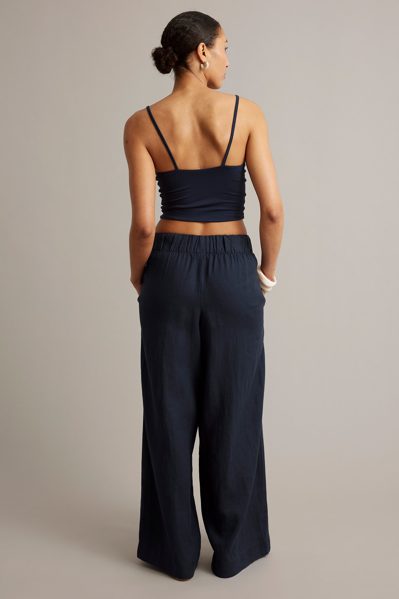 Kvinna bär mörkblå linnebyxor med resår i midjan, sidfickor och en mörkblå camisole.