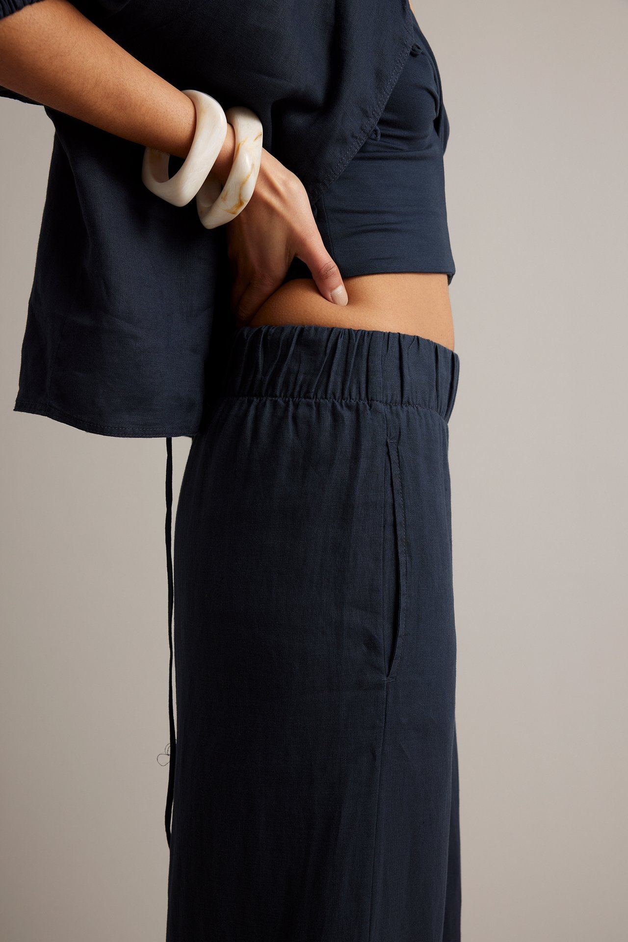 Sidovy: Kvinna i mörkblå linnebyxor med resår i midjan och sidfickor, matchande topp och vita armband.