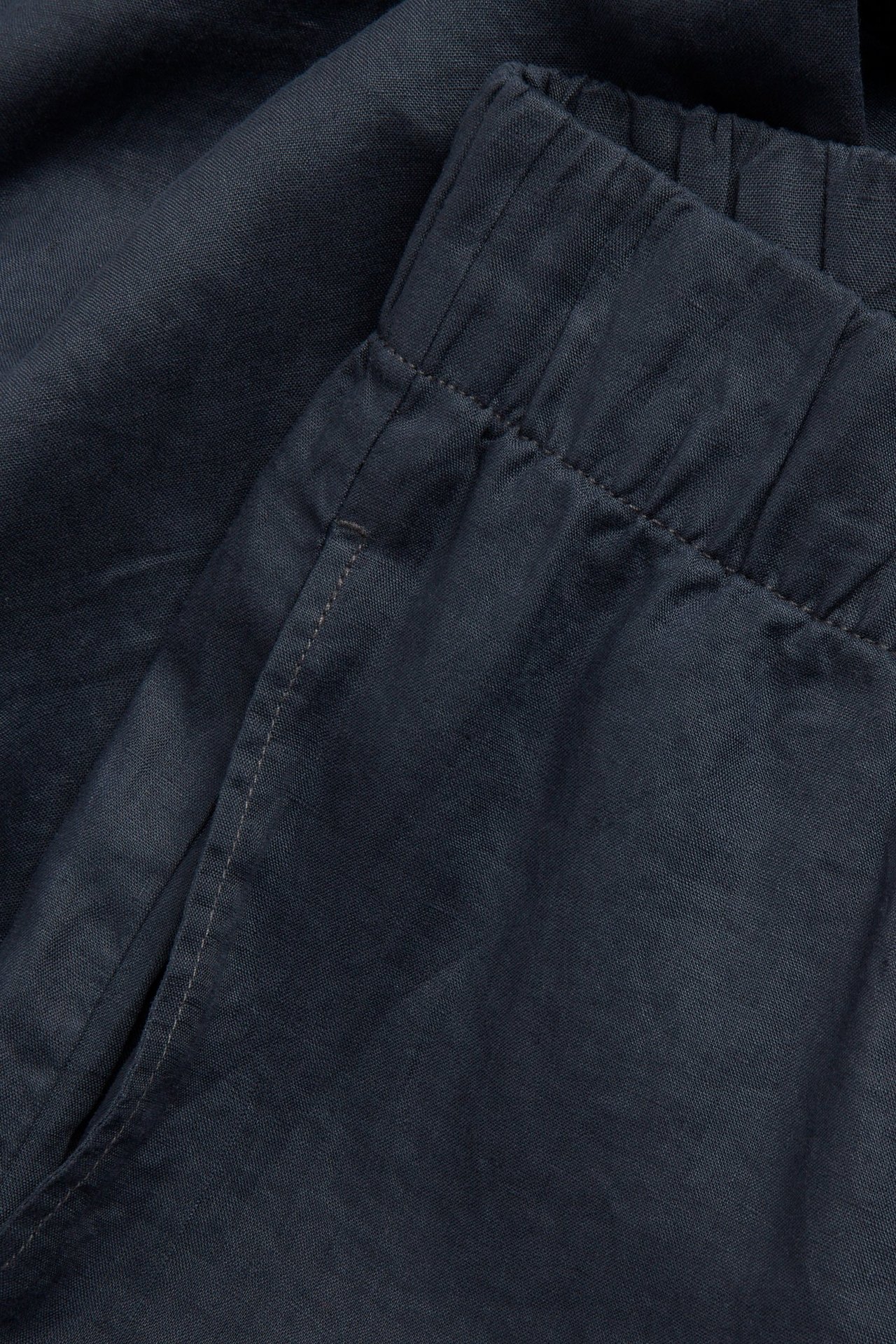 Zbliżenie na ciemnoniebieskie lniane spodnie z elastycznym pasem i boczną kieszenią.