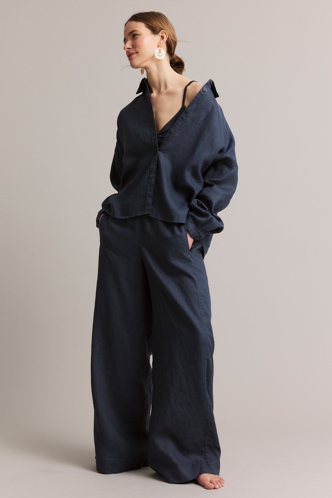 Frontvisning: Kvinne i mørkeblå rette linbukser, matchende linskjorte og hvite øredobber.