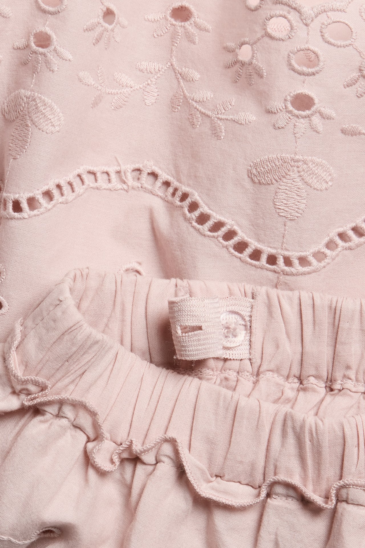 Närbild av en rosa broderad kjol med blommiga utskärningar, justerbar resår i midjan och en liten volang.