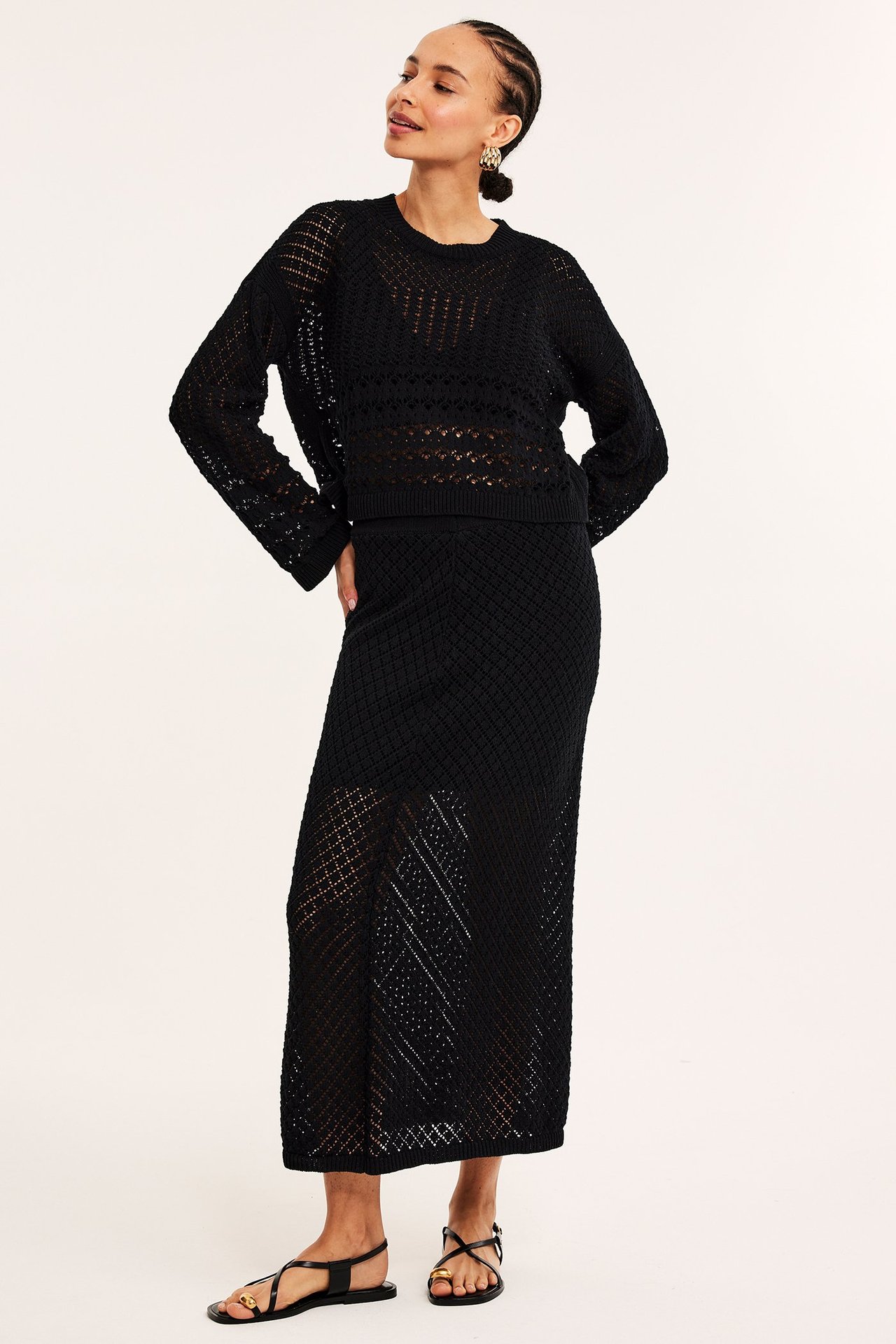Frontbilde av kvinne i svart mønsterstrikket genser, matchende maxiskjørt og svarte flate sandaler.