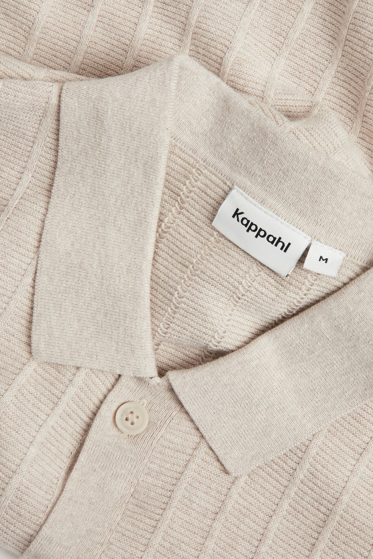 Zbliżenie beżowego melanżowego, krótko rękawowego swetra męskiego z dzianiny ze wzorem strukturalnym i kołnierzem na guziki.