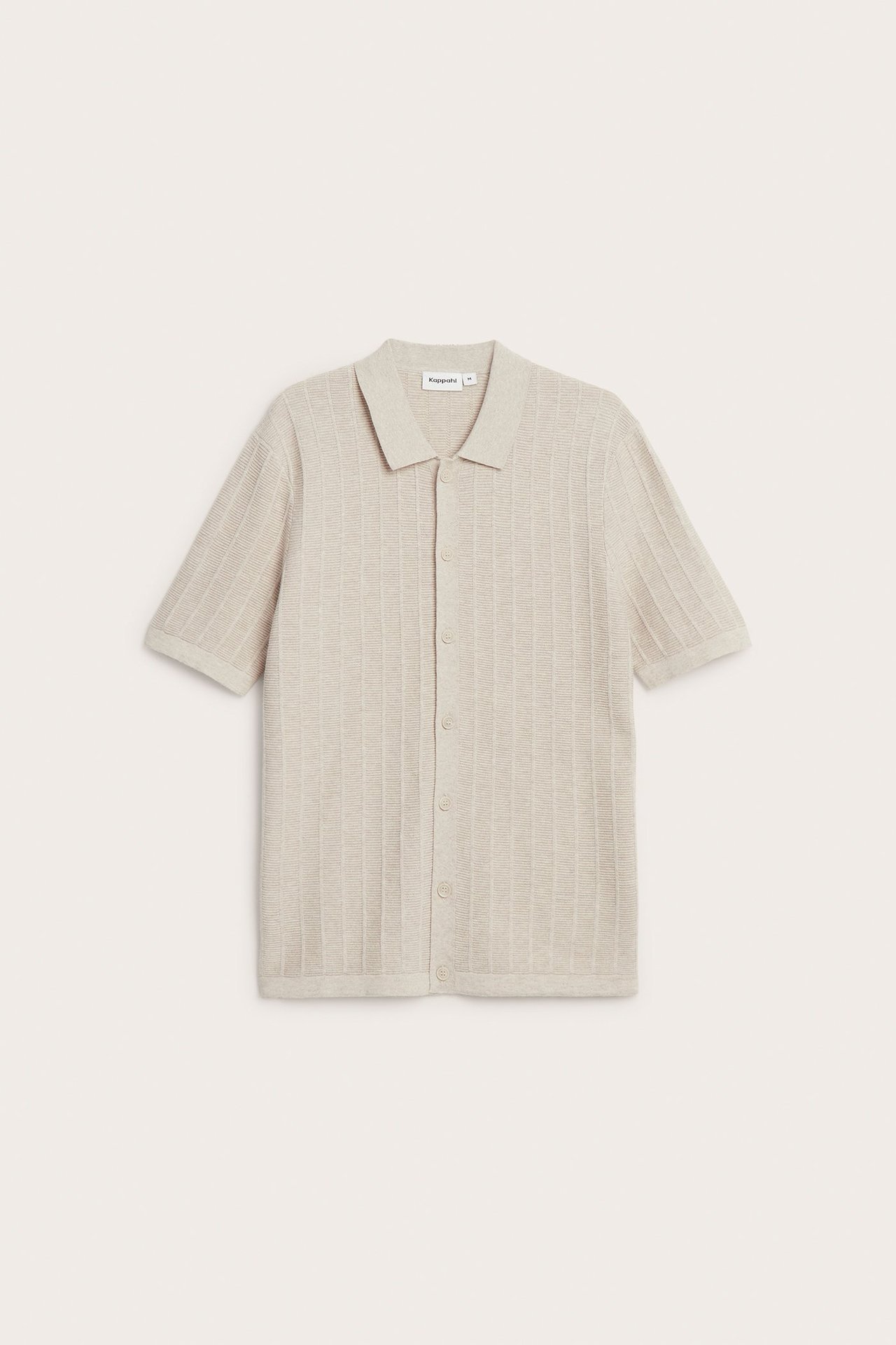 Edestä kuvattu beigenvärinen lyhythihainen neulottu pikeepaita, jossa on kuvioitu pinta ja nappikiinnitys.