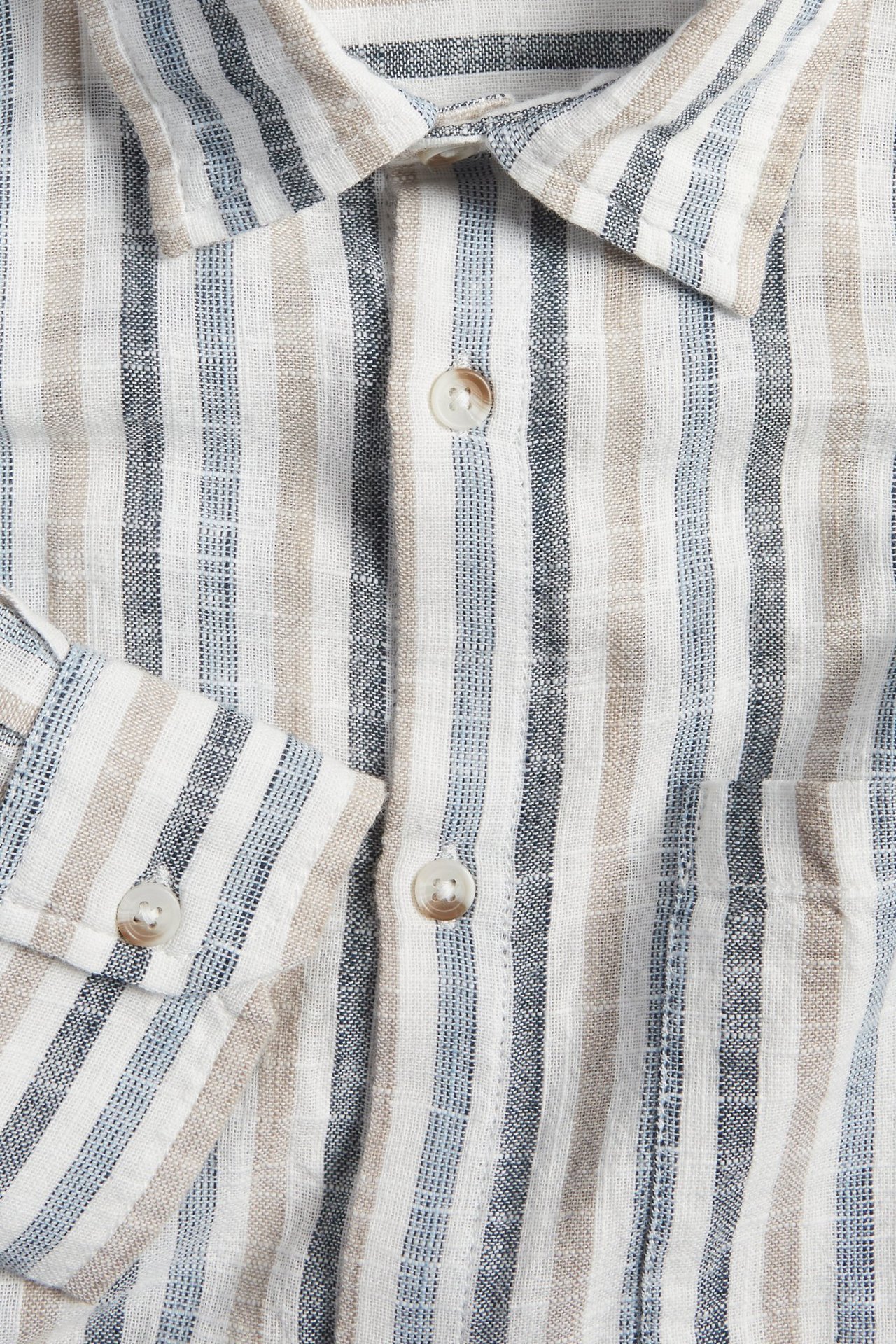 Zbliżenie męskiej koszuli w paski z bawełny, z białymi, jasnoniebieskimi, beżowymi pionowymi paskami i jasnymi guzikami.