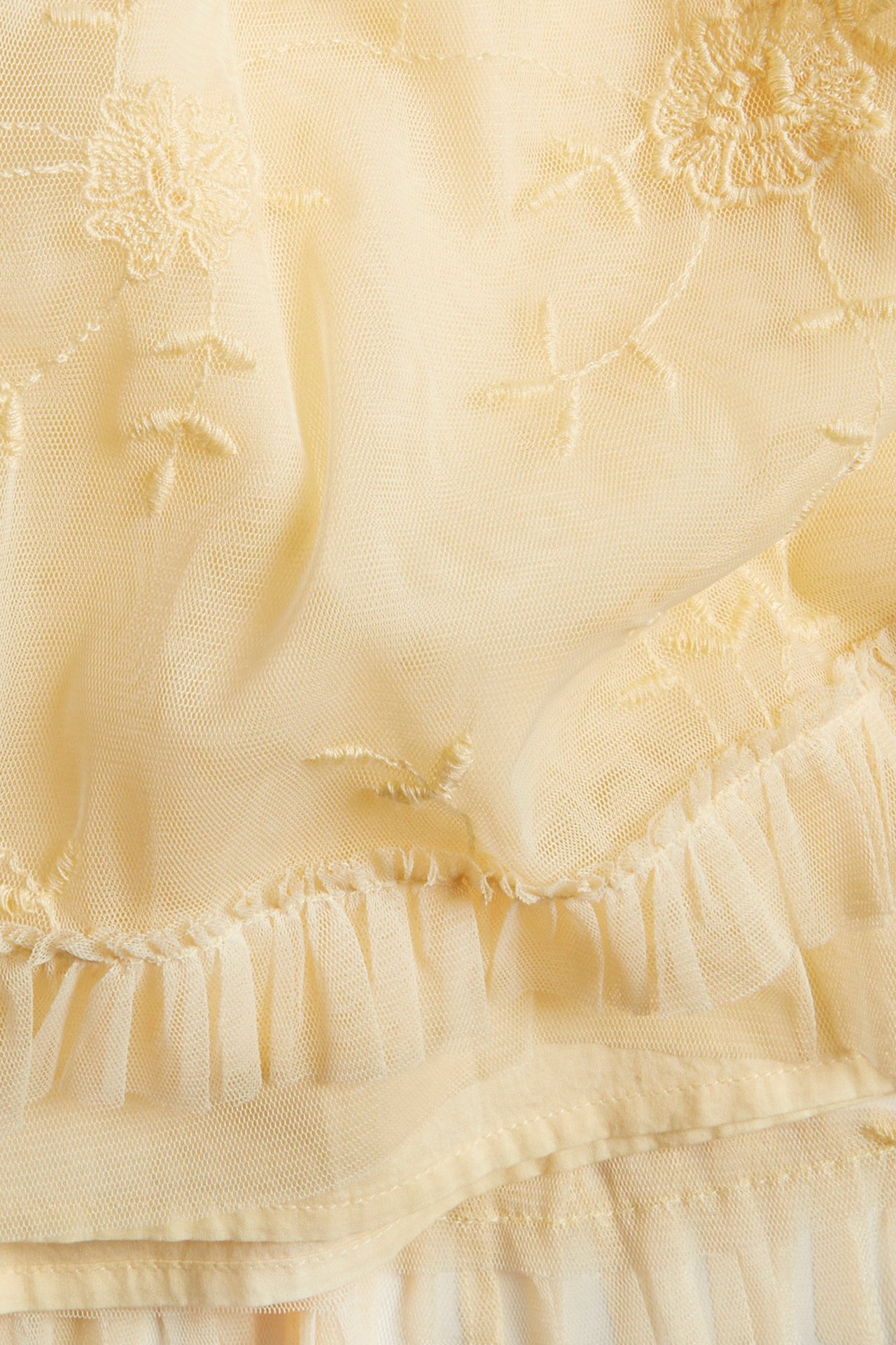 Zbliżenie na jasnożółty, prześwitujący materiał sukienki z haftem kwiatowym i marszczoną falbanką.