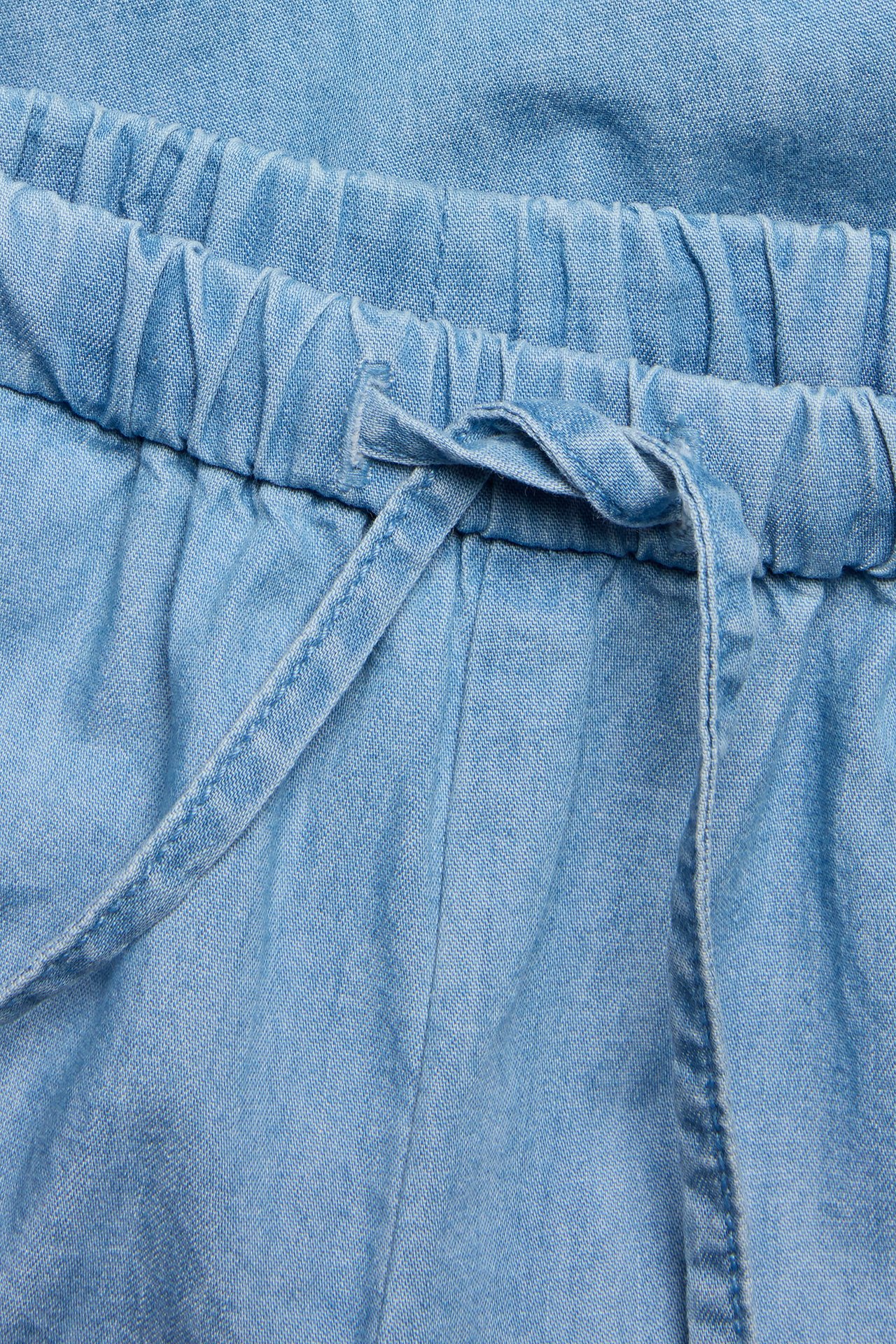 Närbild av ljusblå byxor i mjuk denim med resår och dragsko i midjan.