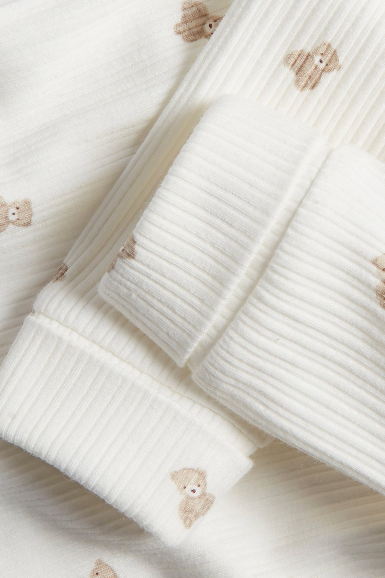 Närbild av offwhite ribbade bomullsleggings med brunt nallemönster och nedvikbara muddar.