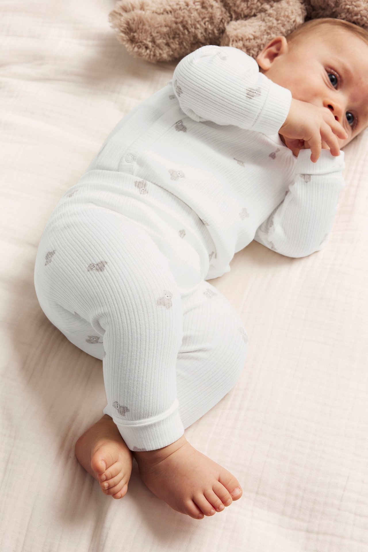 Uppifrån, baby i offwhite ribbade leggings och matchande långärmad topp med nallemönster.