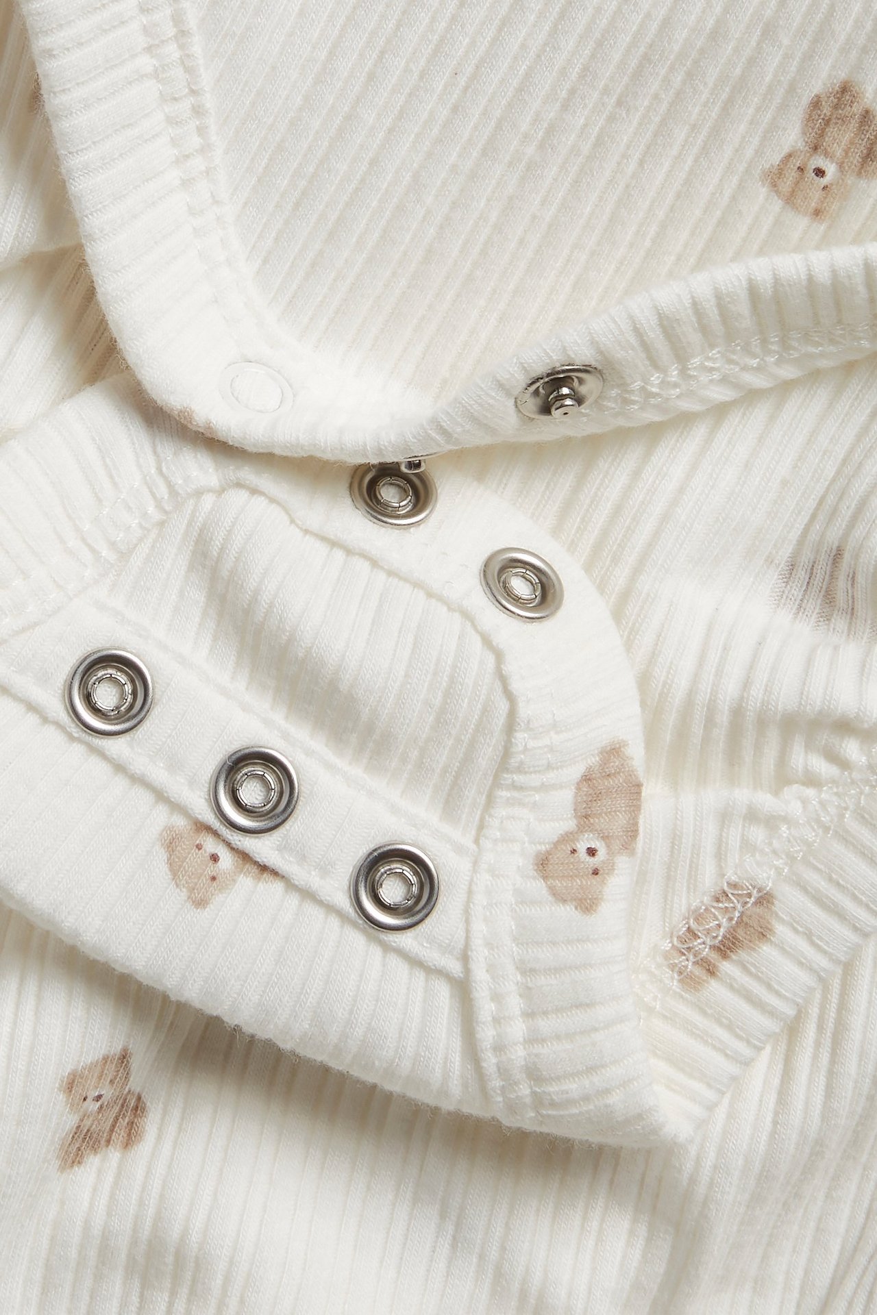 Närbild på en offwhite ribbad babybody med nallemönster och tryckknappar.