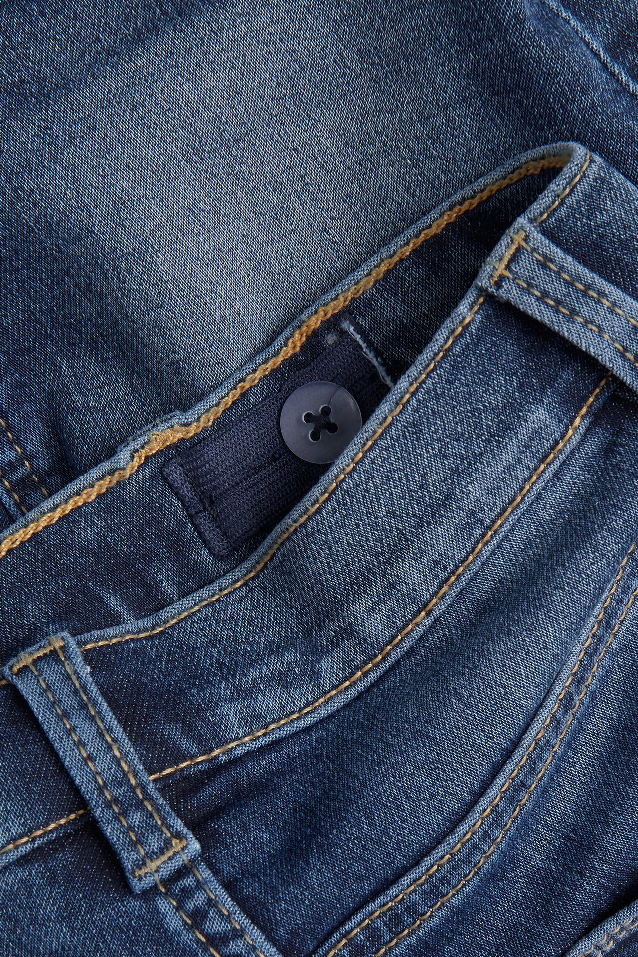 Lähikuva sinisten denimshortsien vyötärönauhasta, jossa säädettävä kuminauha ja nappi.