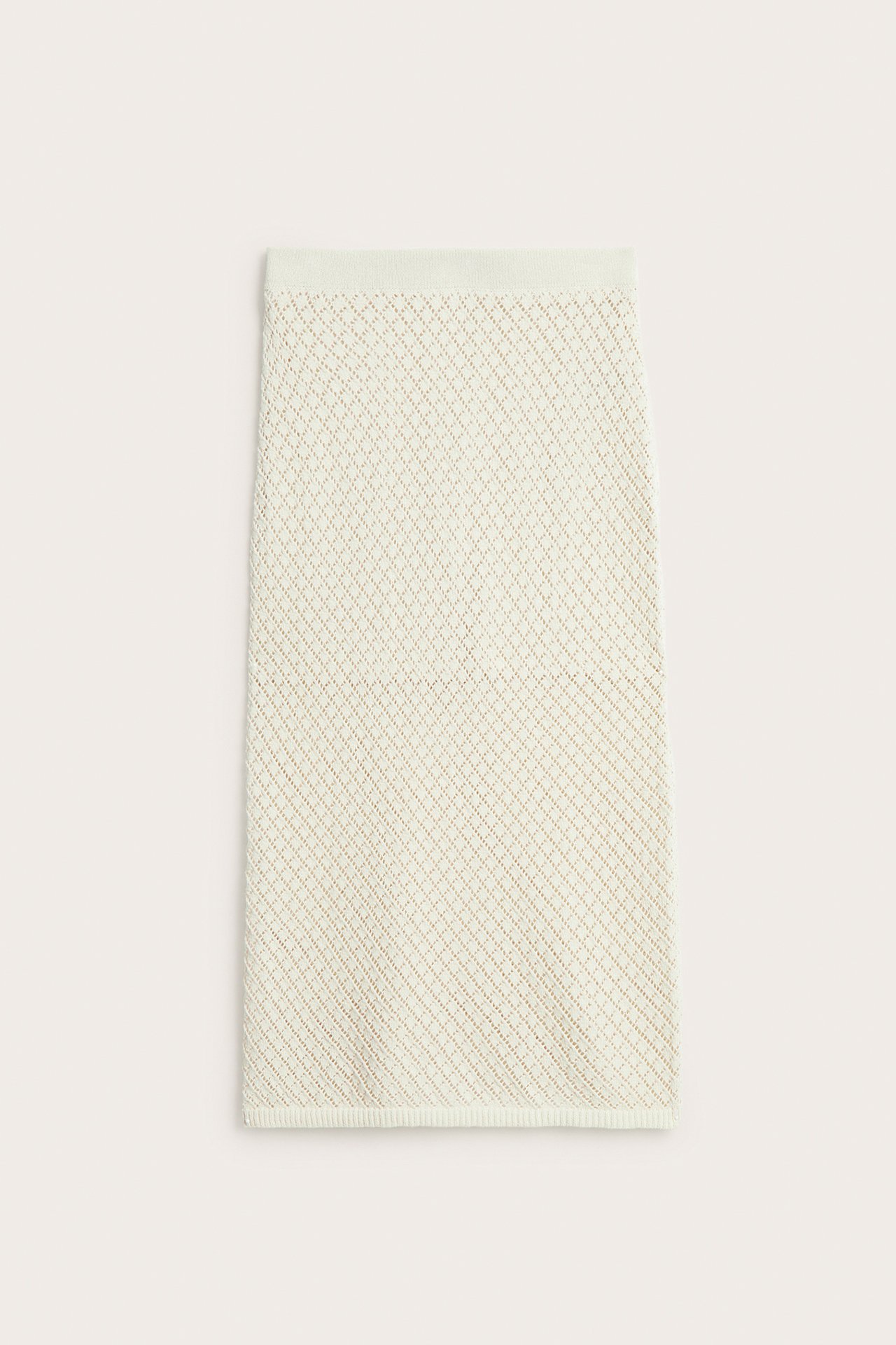 Framifrån, ljusbeige stickad lång kjol med diamantformat spetsmönster.