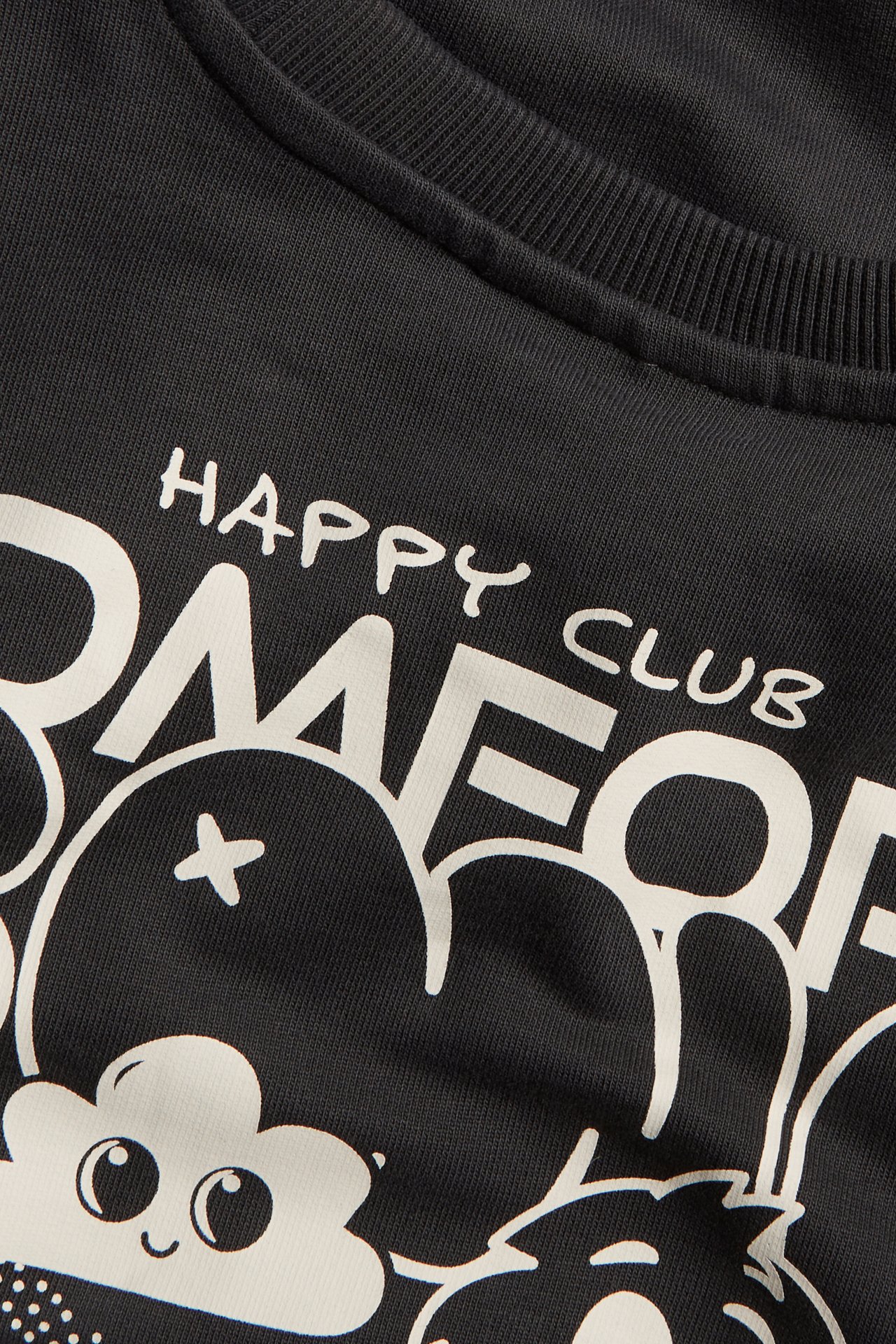 Närbild på en svart bomullssweatshirt för barn med vitt grafiskt tryck och texten 'HAPPY CLUB'.