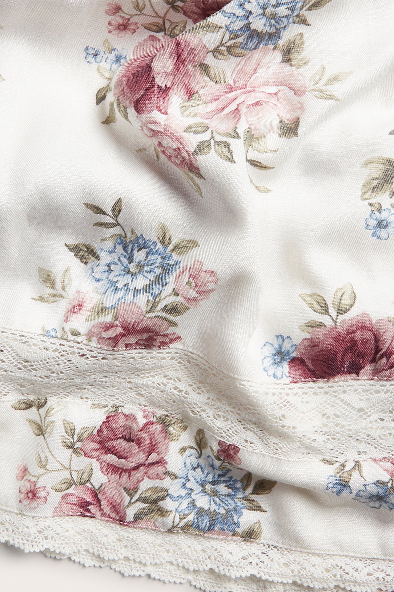 Närbild av en offwhite blommig viskos twillkjol med rosa och blå blommor och spetsdetaljer.