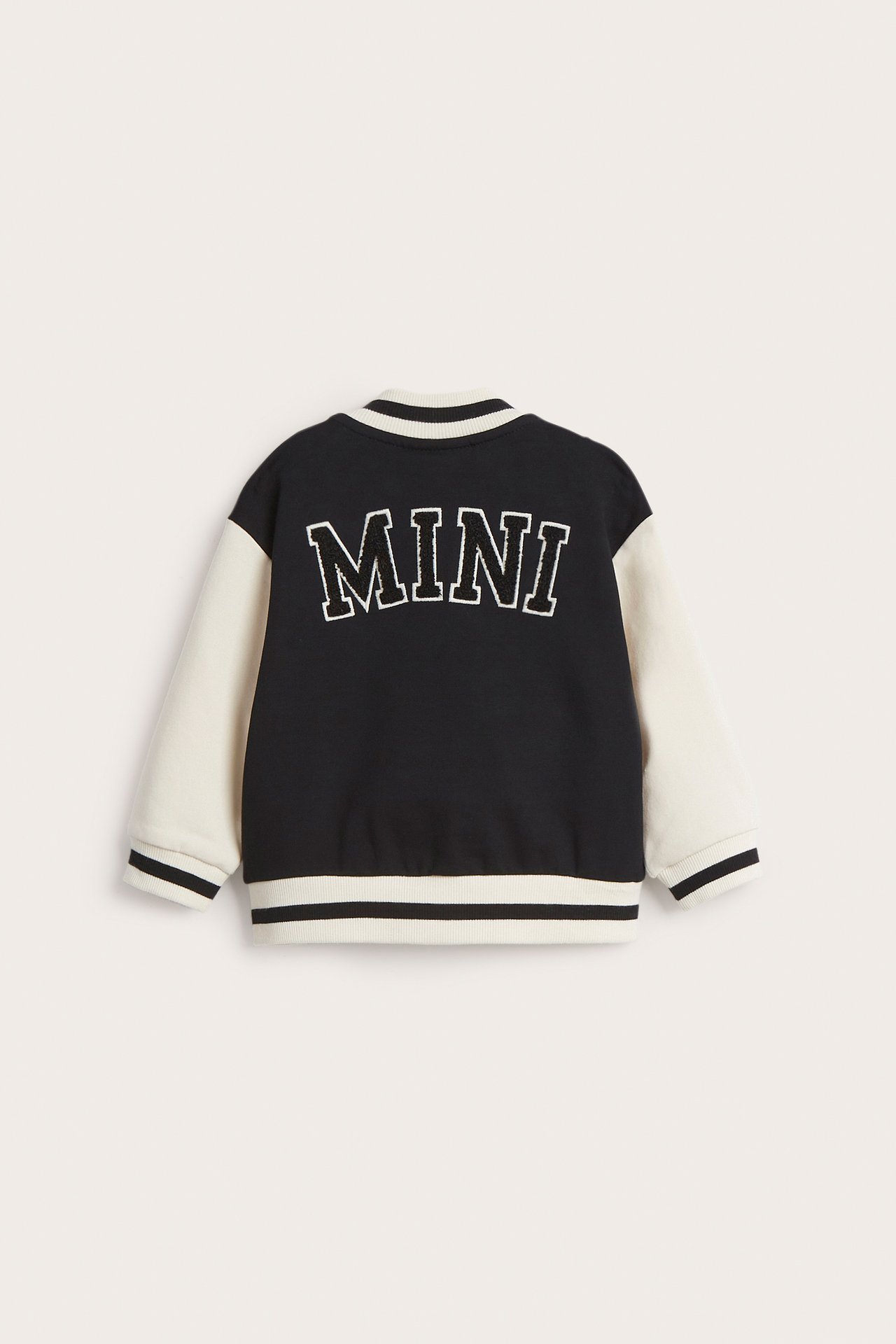 Takaa: vauvan musta ja vaaleanbeige baseball-takki, jossa "MINI" froteeapplikaatio.