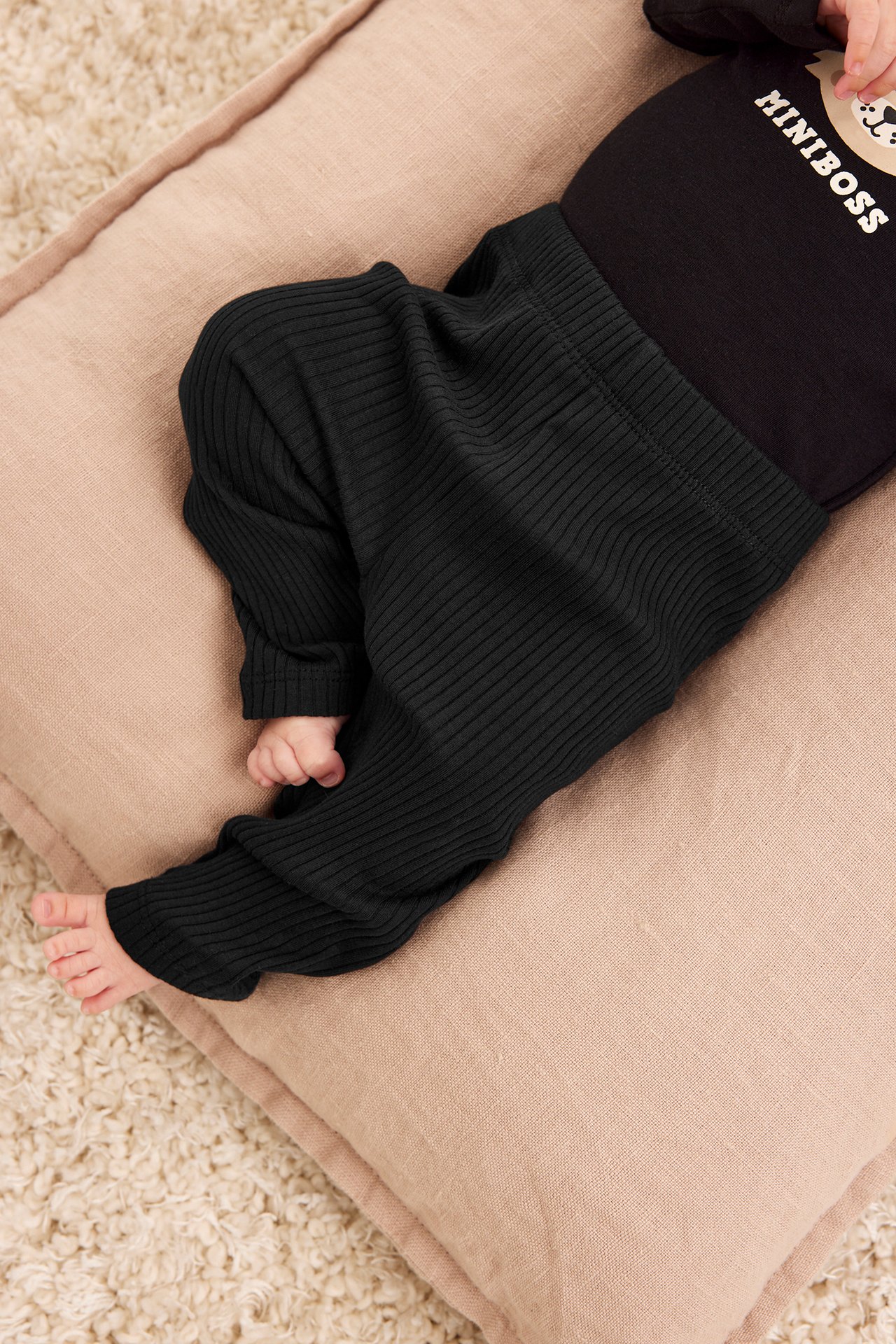 Uppifrån-vy av en baby i svarta ribbade leggings och en svart 'MINIBOSS' body.