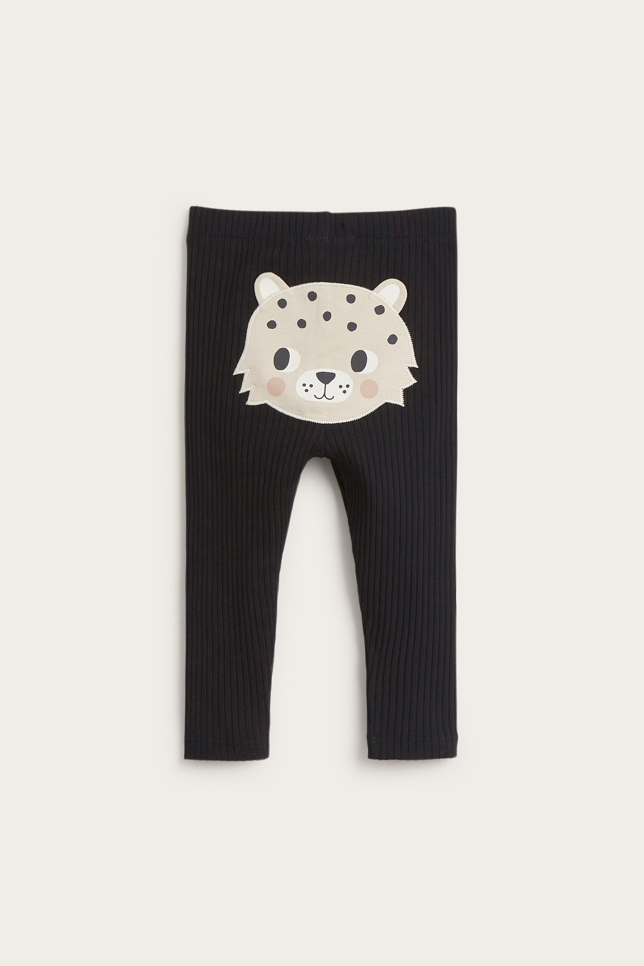 Frontvy av svarta ribbade baby-leggings med en ljusbeige leopardansiktsapplikation.