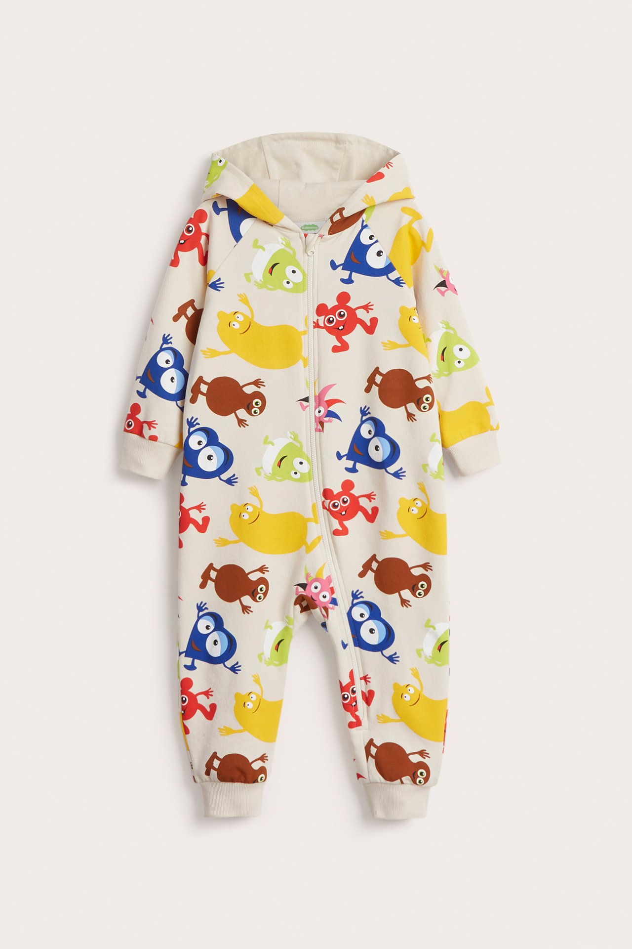 Framifrån, ljusbeige mönstrad babyjumpsuit med Babblarna-tryck, huva och dragkedja fram.