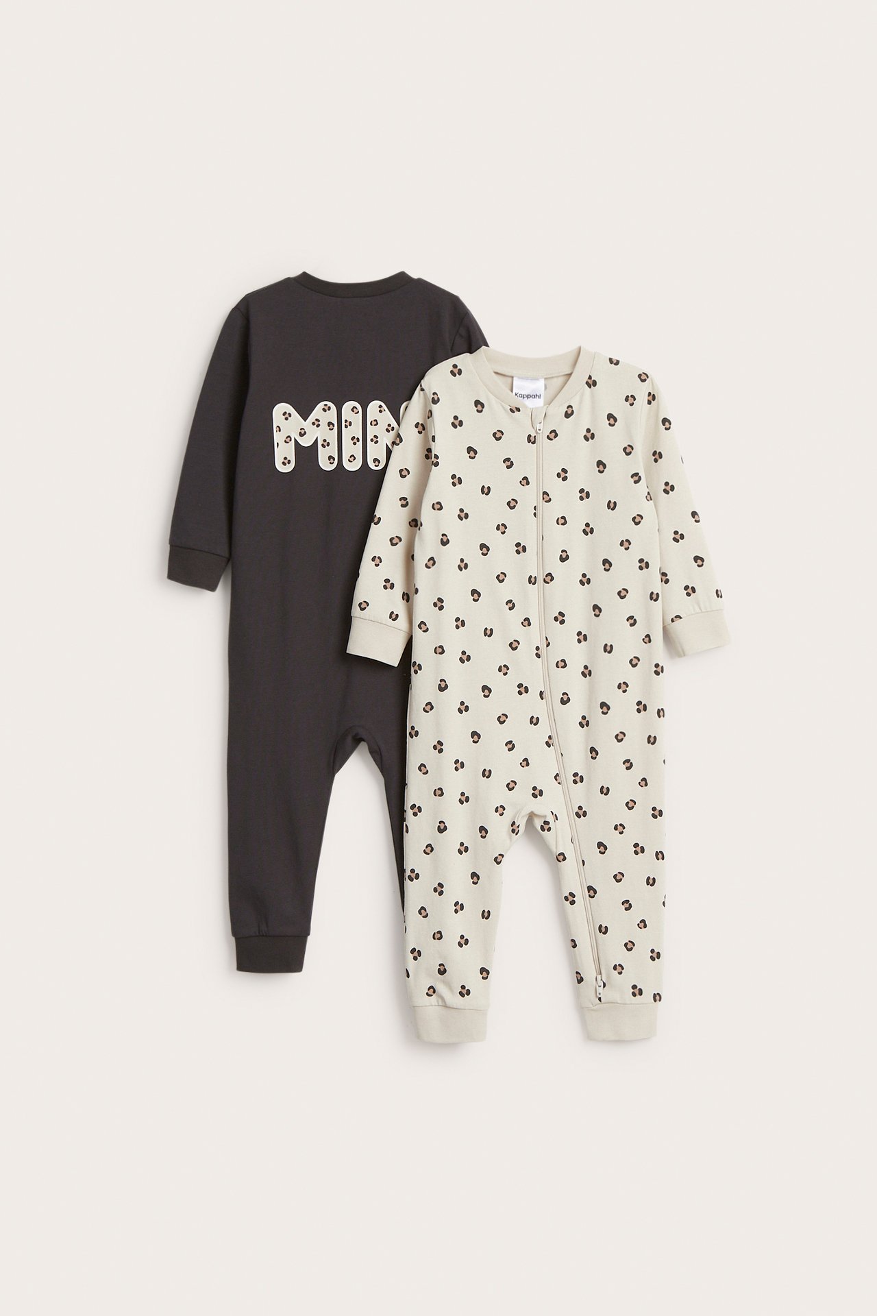 Framifrån: två långärmade baby-pyjamasar. En beige mönstrad med tvåvägsdragkedja, och en mörkgrå med 'MINI'-tryck.