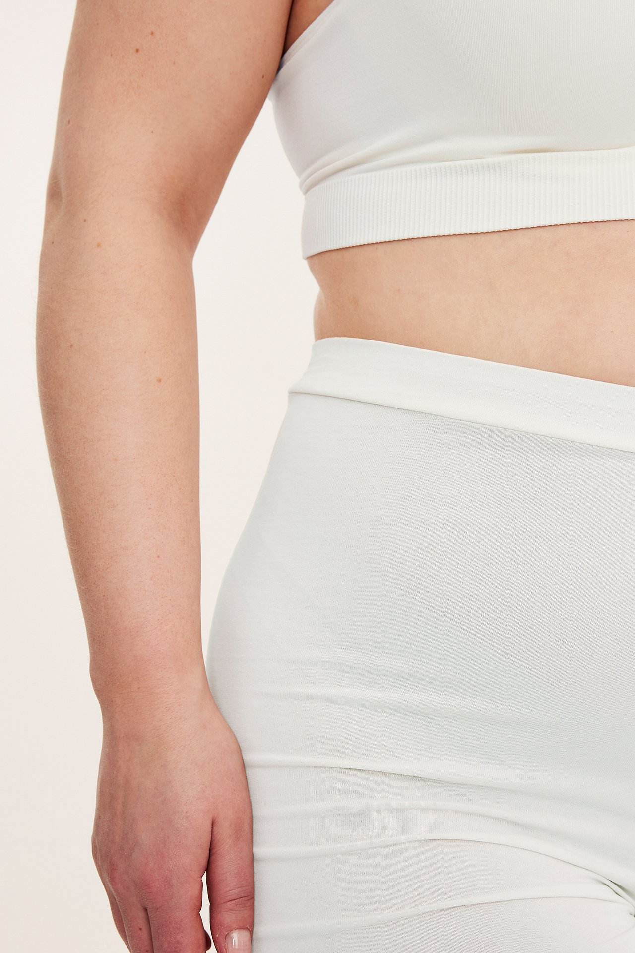Närbild, sidovy av en kvinna i offwhite mjuka shorts och en matchande ribbad bralette.