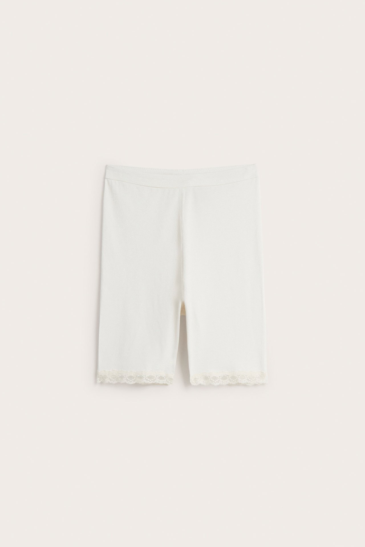 Frontvy av offwhite mjuka bomullsshorts med resår i midjan och delikat spetskant.