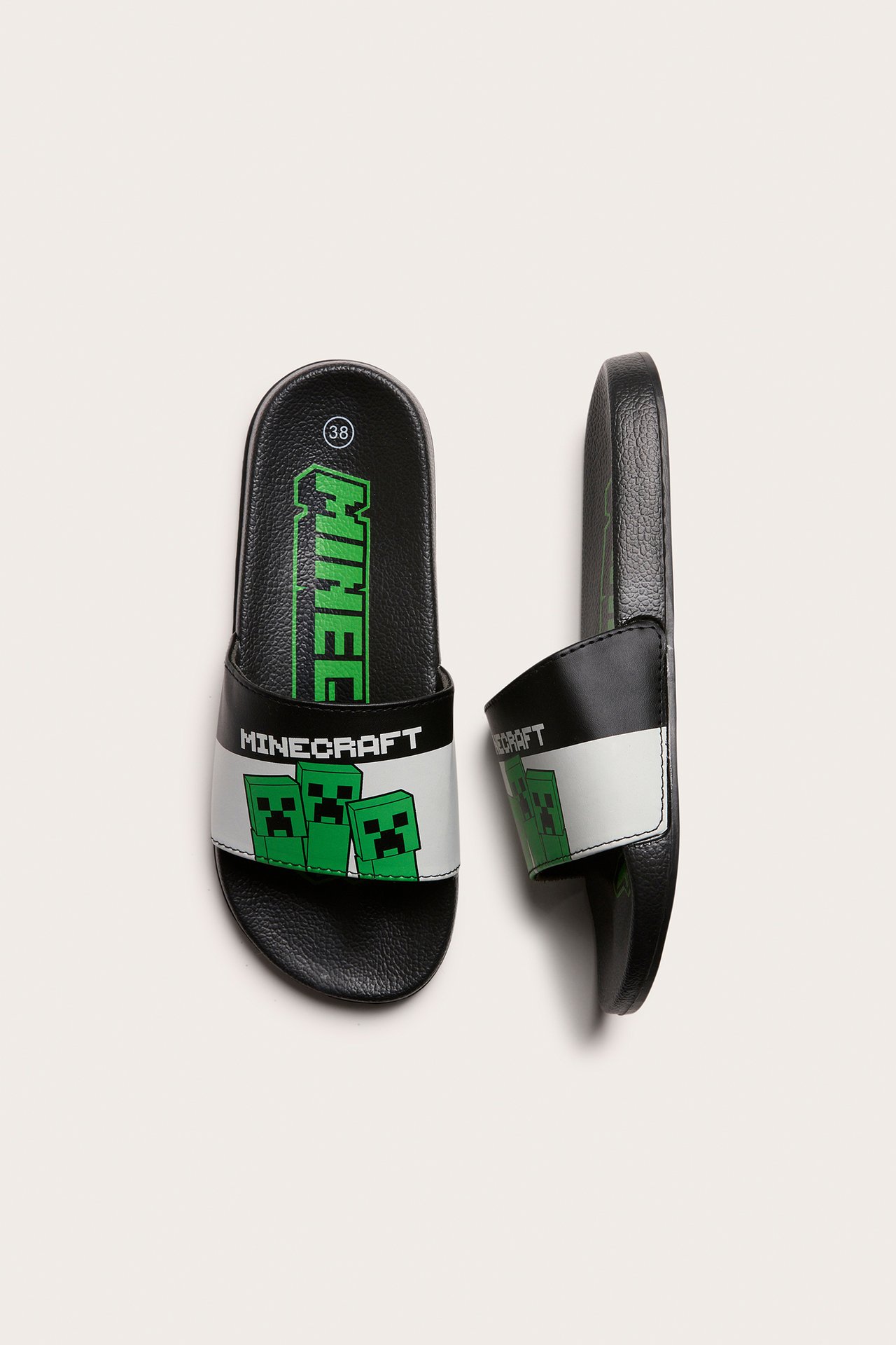 Ovanifrån: Svarta barnsandaler med vit rem, grönt Minecraft-logga och Creeper-ansikten.