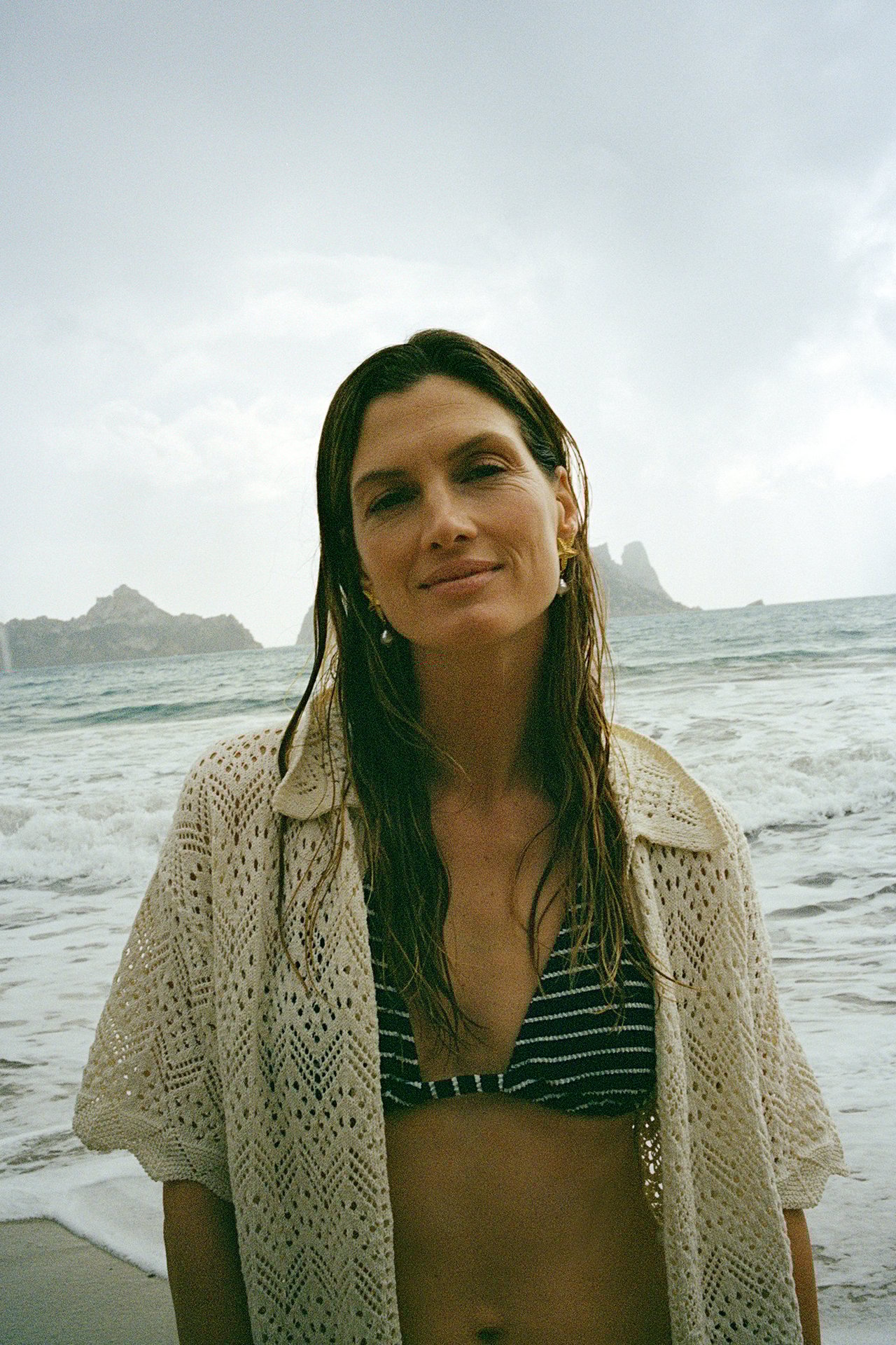 Edestä kuvattu nainen yllään vaaleanbeige lyhythihainen avoin neulejakku raidallisen bikinitopin päällä.