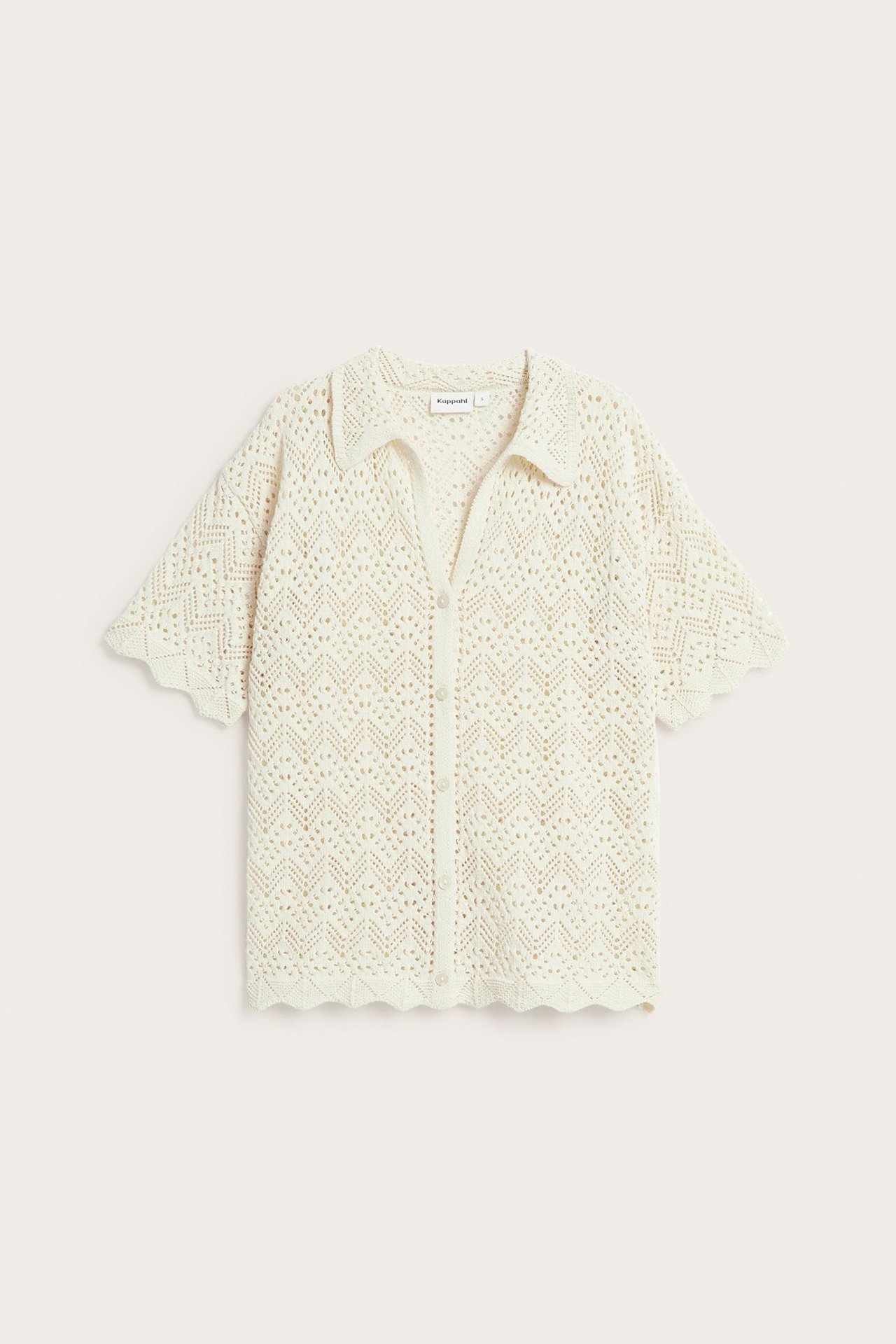 Edestä: Vaaleanbeige lyhythihainen avoneuletakki, jossa kaulus, napit ja aaltoilevat reunat.