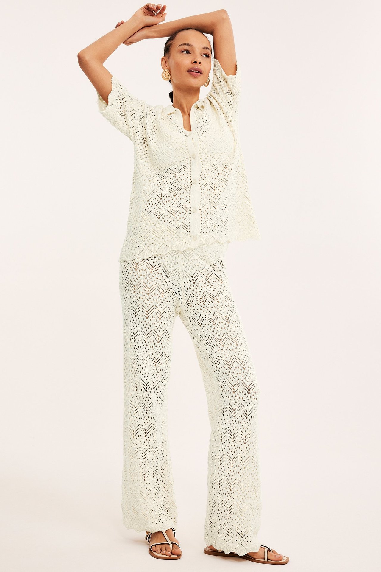 Edestä: nainen yllään vaaleanbeiget leveälahkeiset neulotut virkatut housut, yhteensopiva paita ja sandaalit.