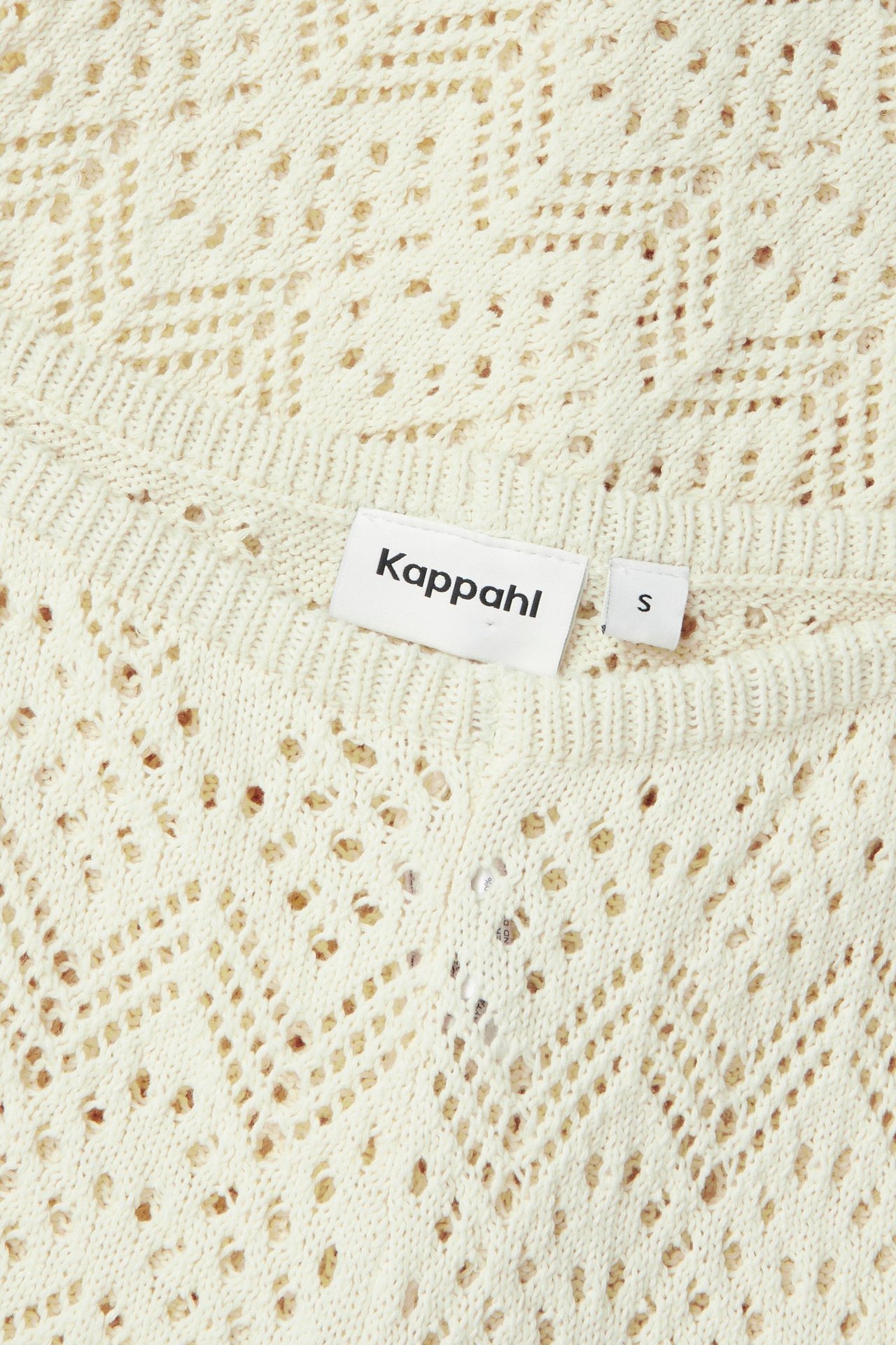 Zbliżenie na jasnobeżowe dzianinowe spodnie szydełkowe, z metką Kappahl i rozmiarem S.
