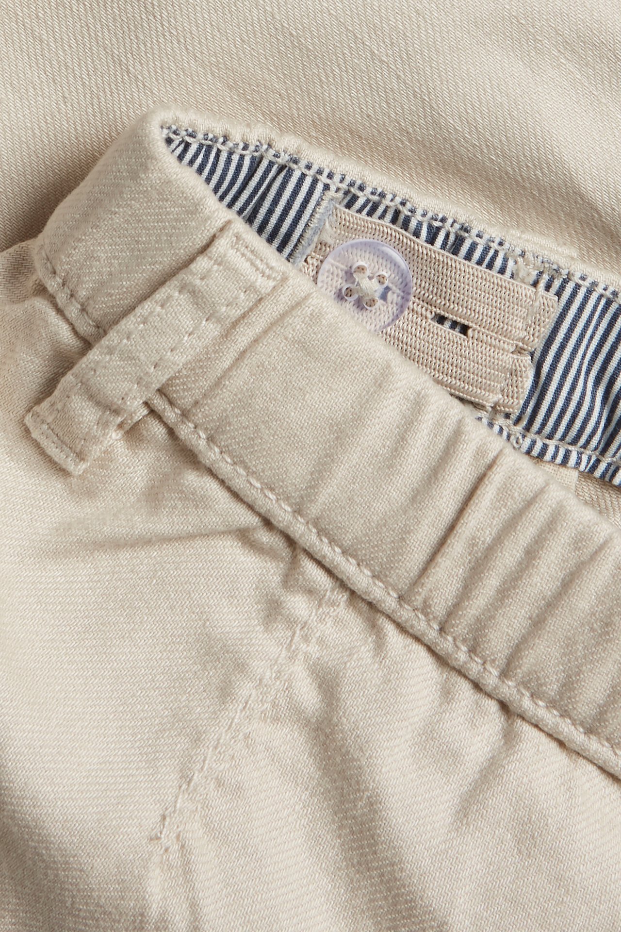 Nærbilde av beige vevde shorts linning med knappelukking, justerbar strikk og stripete fôr.