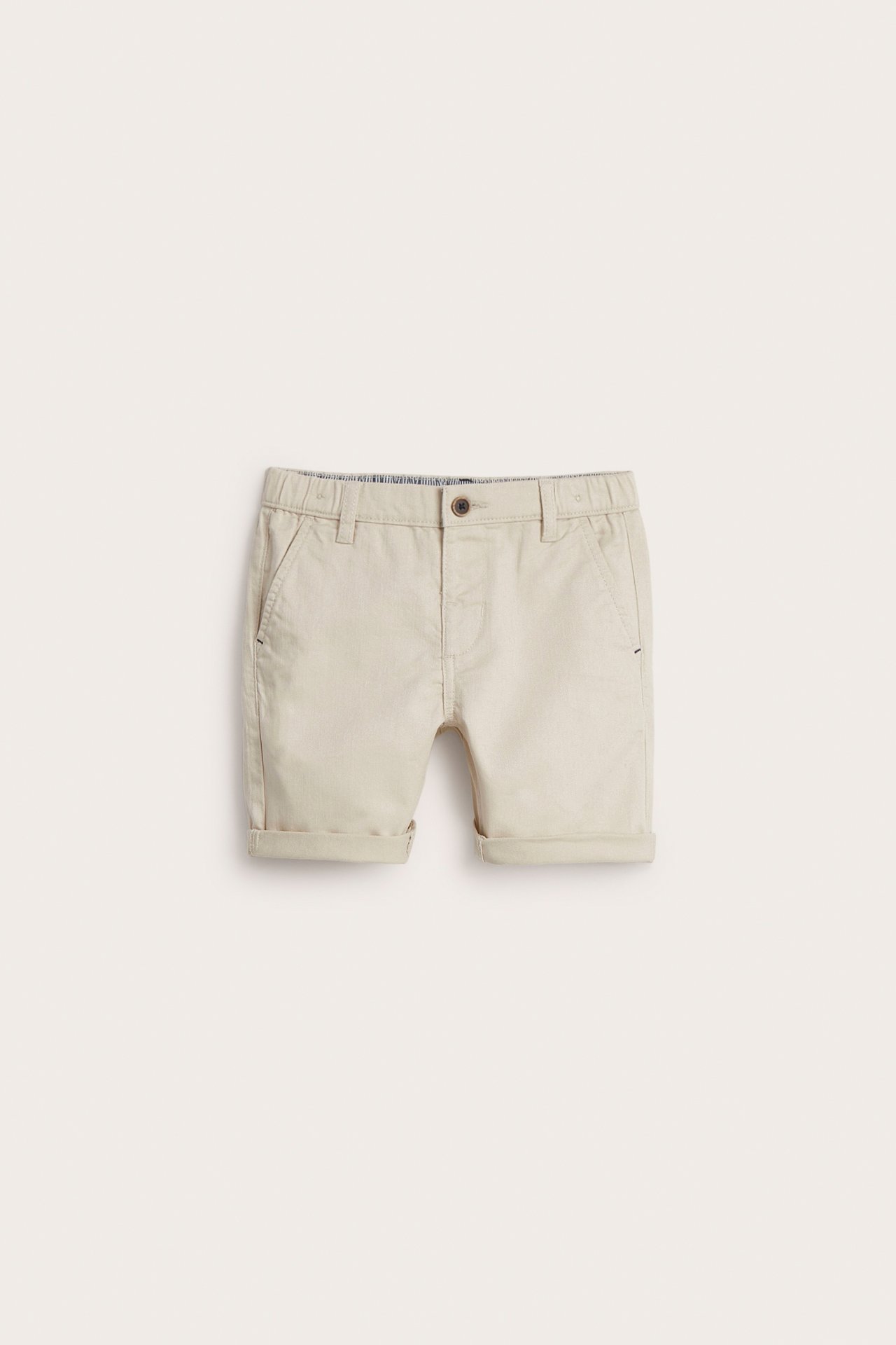 Frontvisning av beige vevde barneshorts med knapp foran, sidelommer og oppbrettede ben.