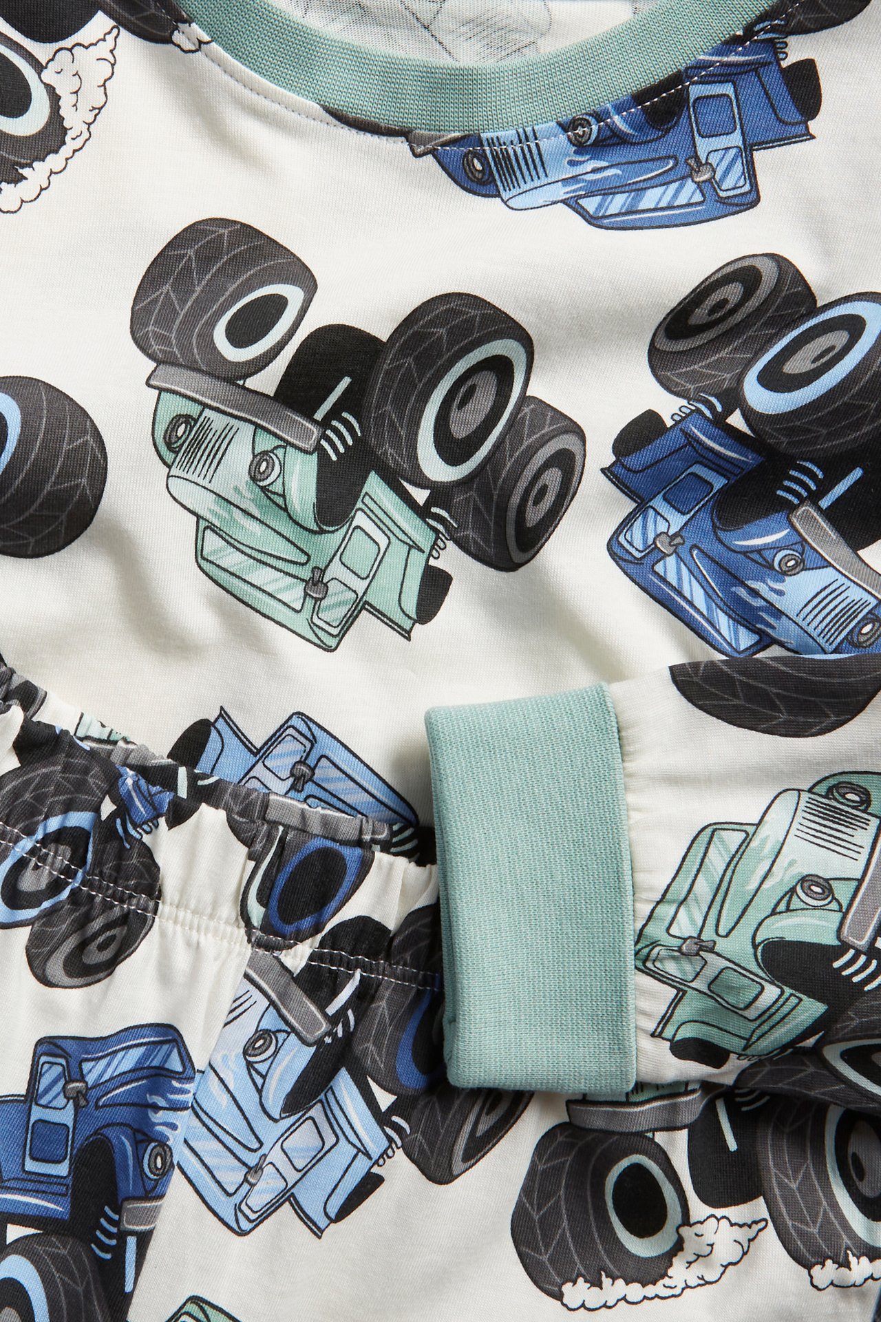 Närbild av en barnpyjamas i benvit bomull med blå monstertruckar och ribbade muddar.