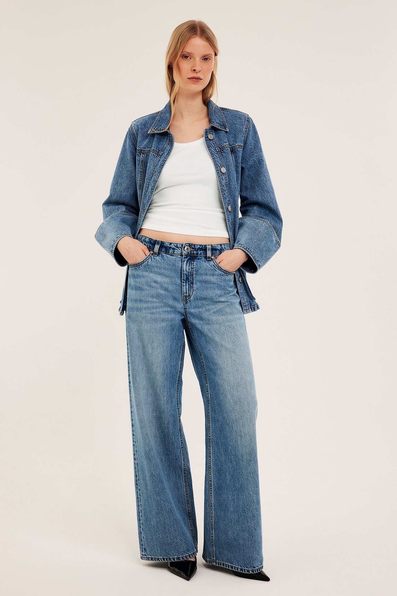 Framsida av kvinna i offwhite ribbat linne, blå jeansjacka och vida jeans.