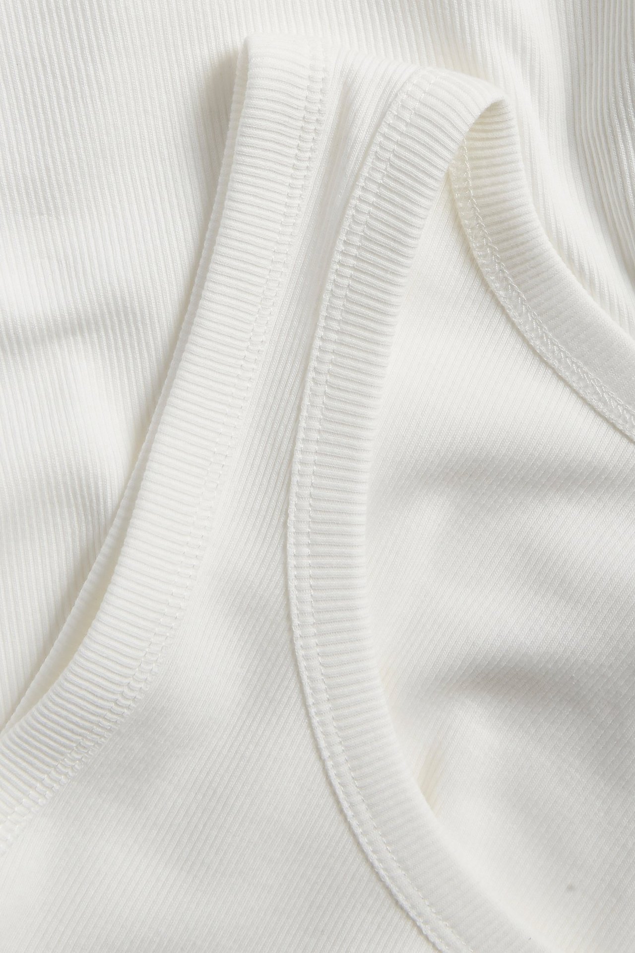 Zbliżenie na biały prążkowany top, ukazujące wąski prążkowany materiał i szwy.